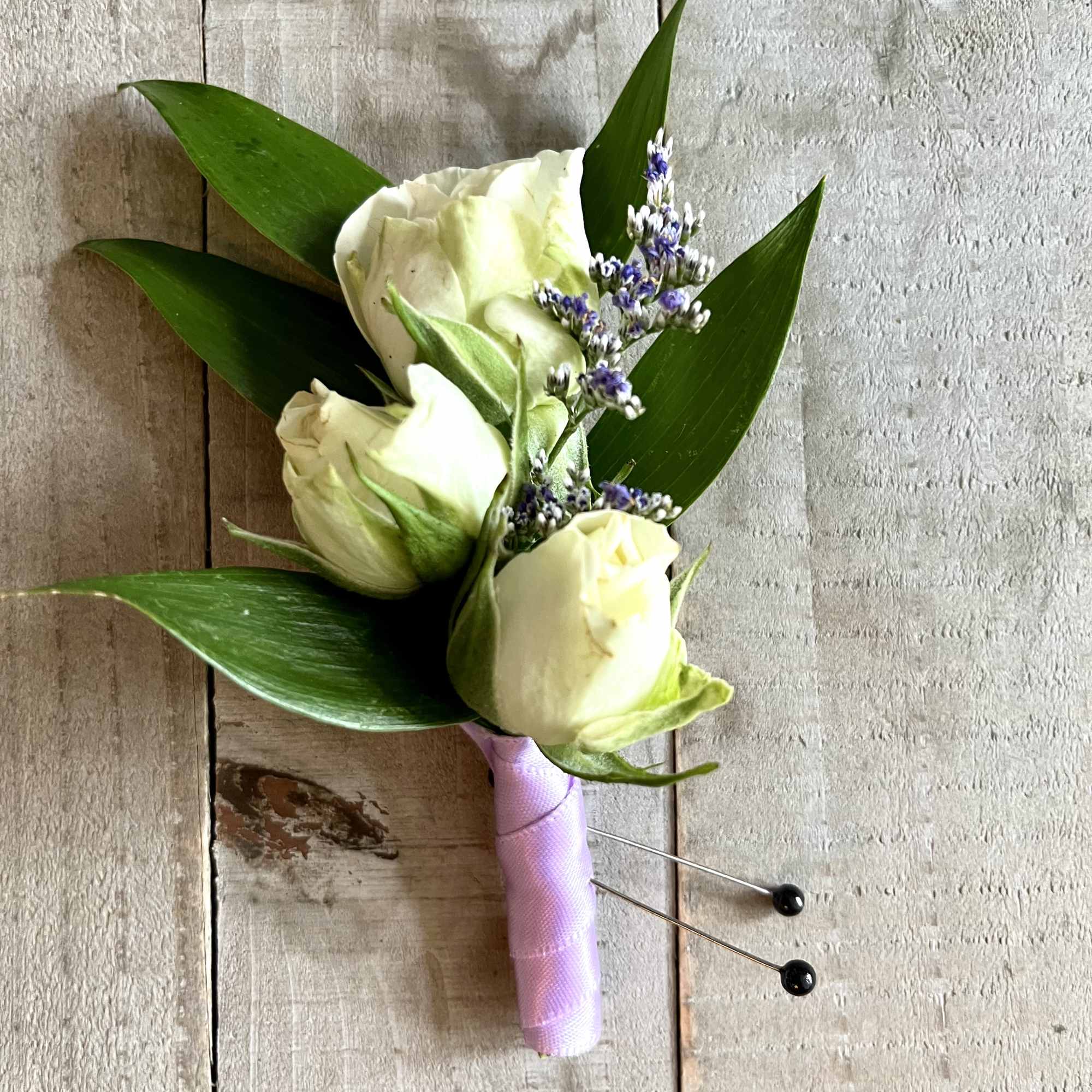 White rose boutonniere with purple accents and green leaves