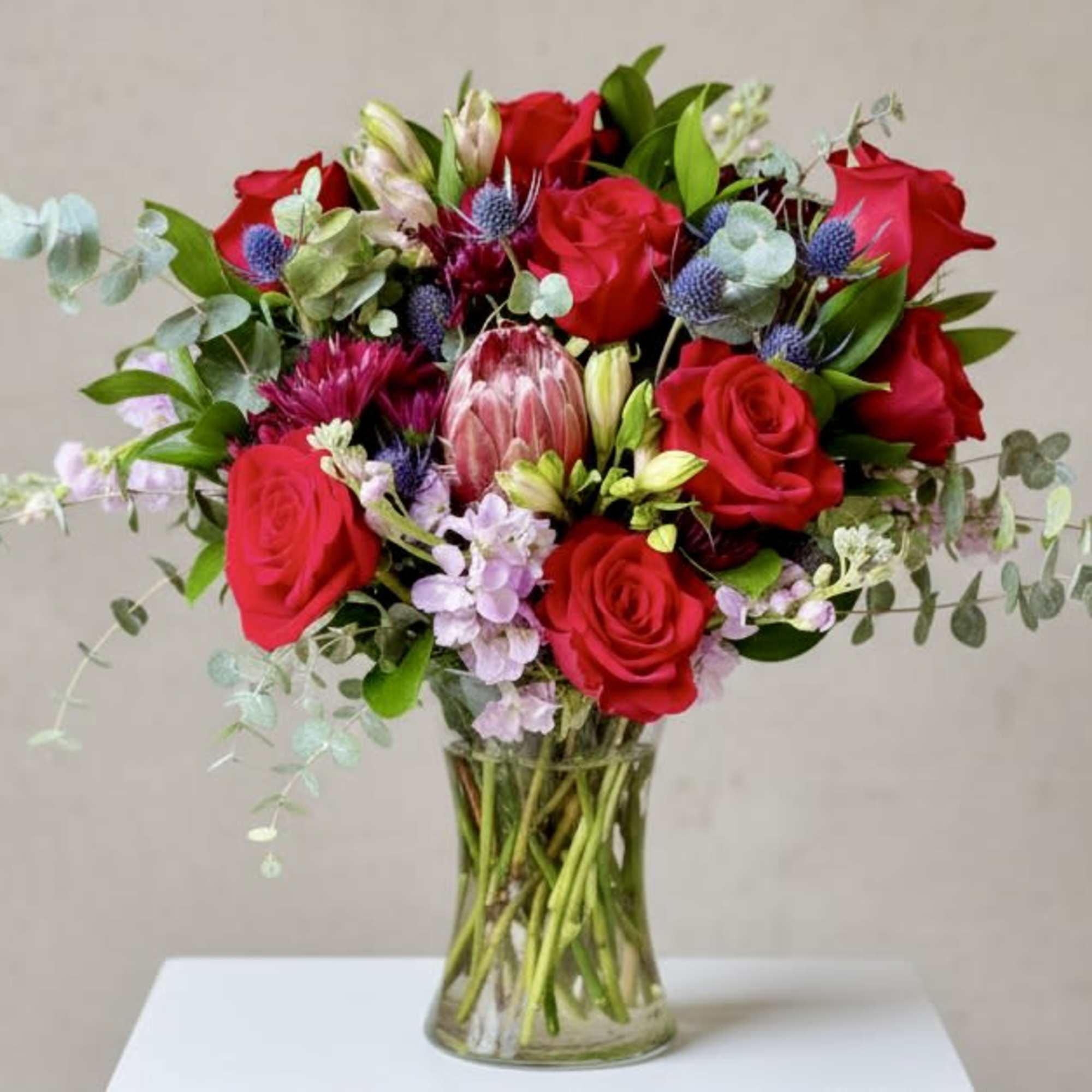 A central pink protea anchors this garden-inspired flower arrangement, surrounded by clusters