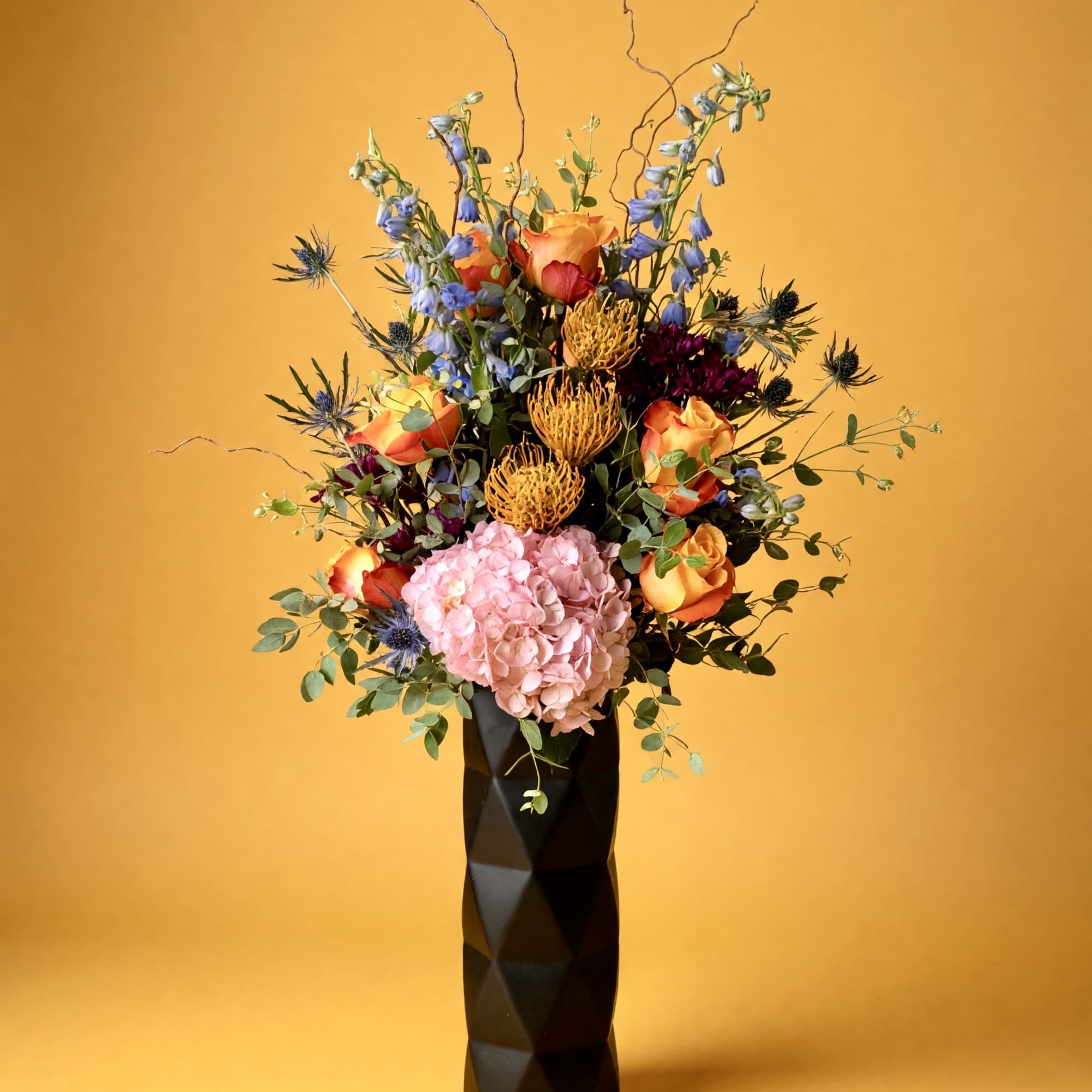 Tall mixed floral arrangement in a black vase with pink hydrangea and orange roses