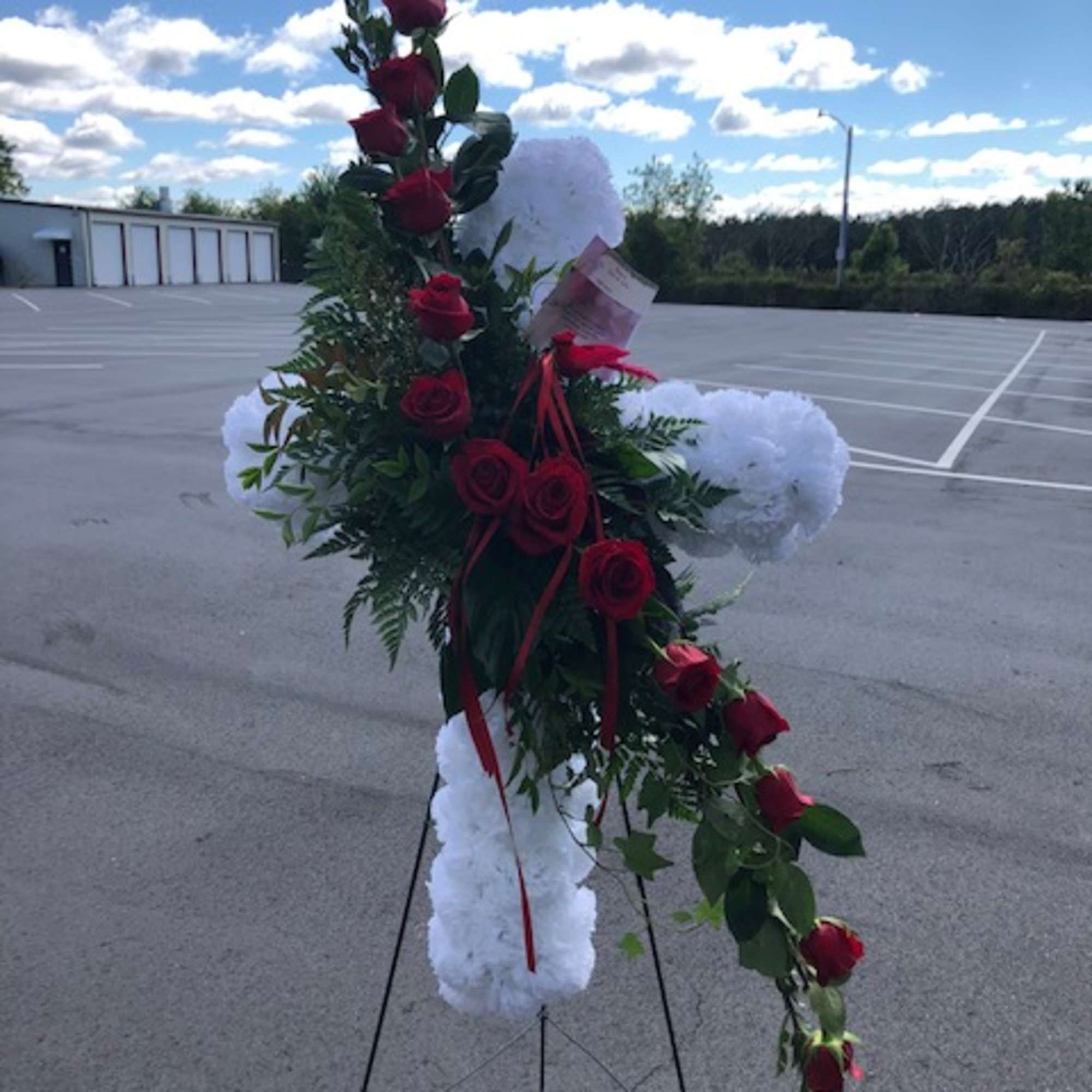 Standing floral spray with red roses and white pom-poms on a metal easel