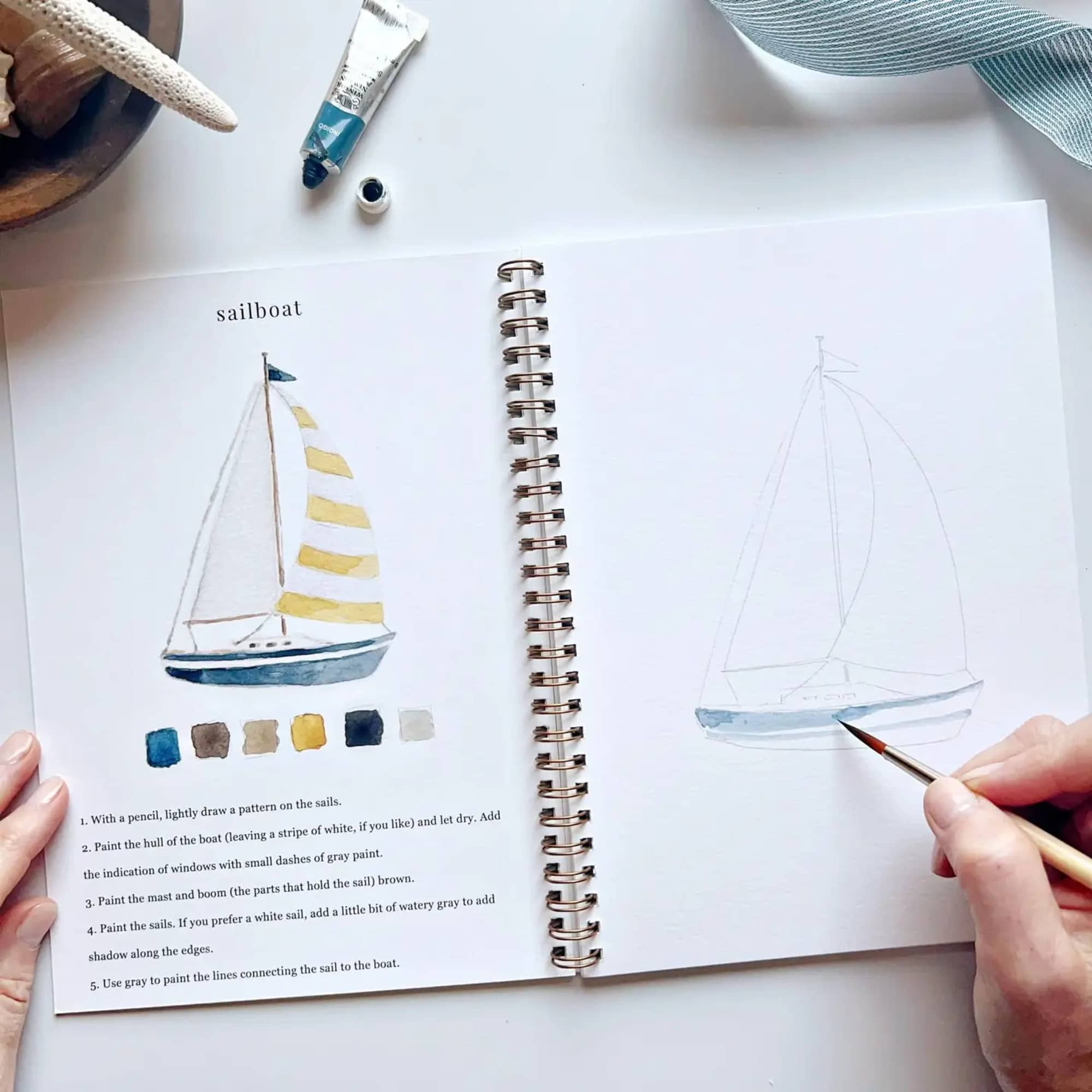 Open sketchbook with watercolor sailboat drawings and a hand painting one page