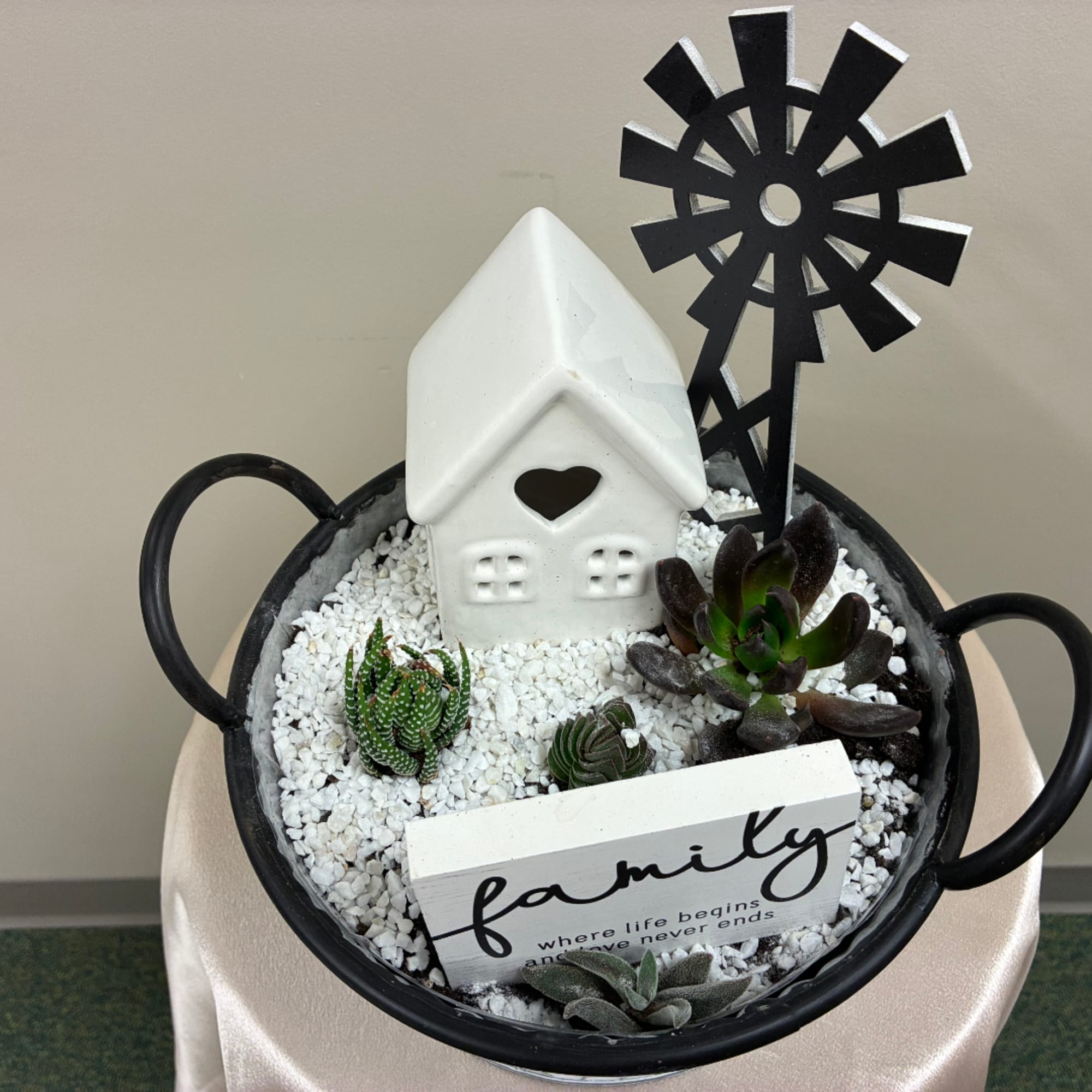 Succulent arrangement in a black handled bowl with a small white house and sign