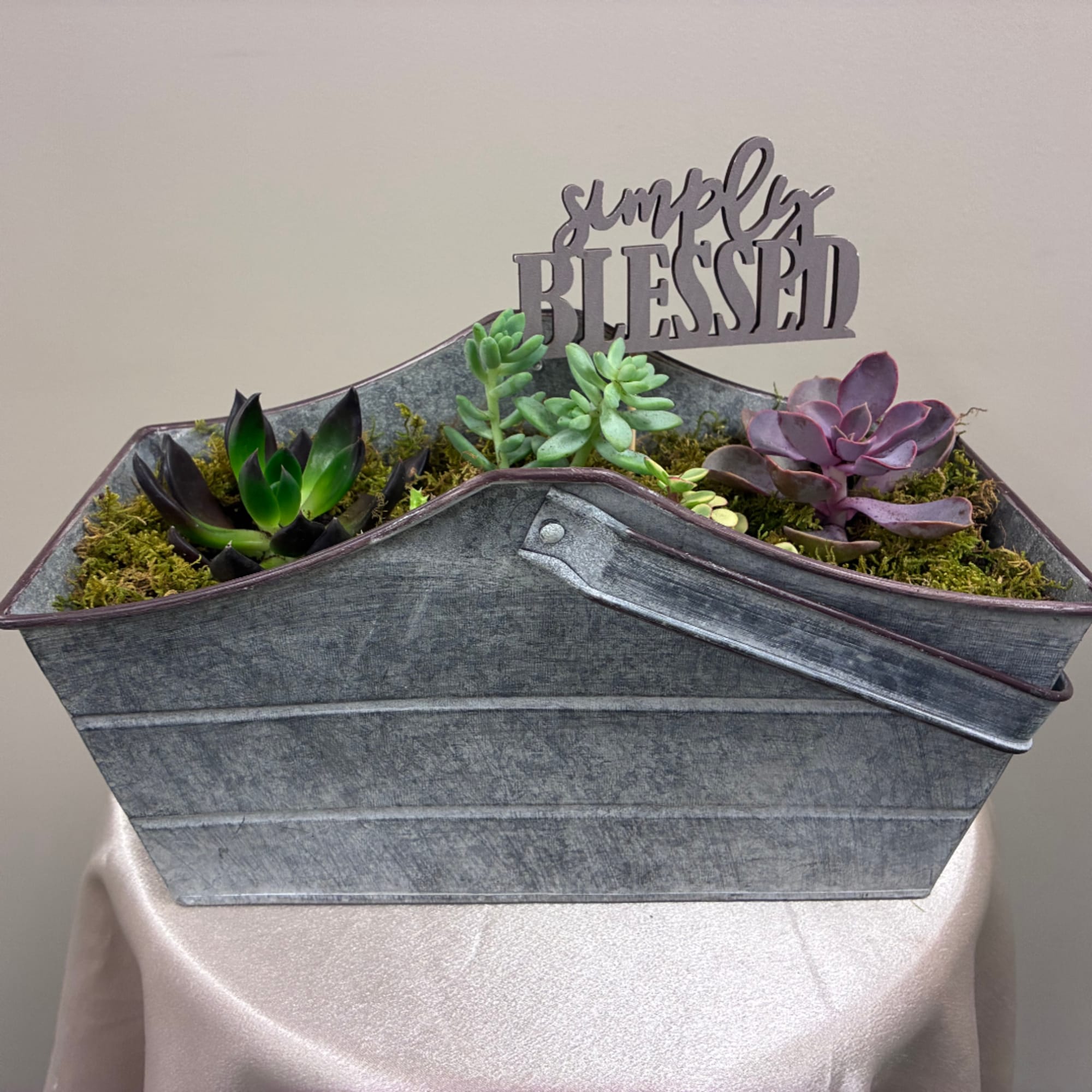 Succulent arrangement in a galvanized metal container with a "simply blessed" sign.