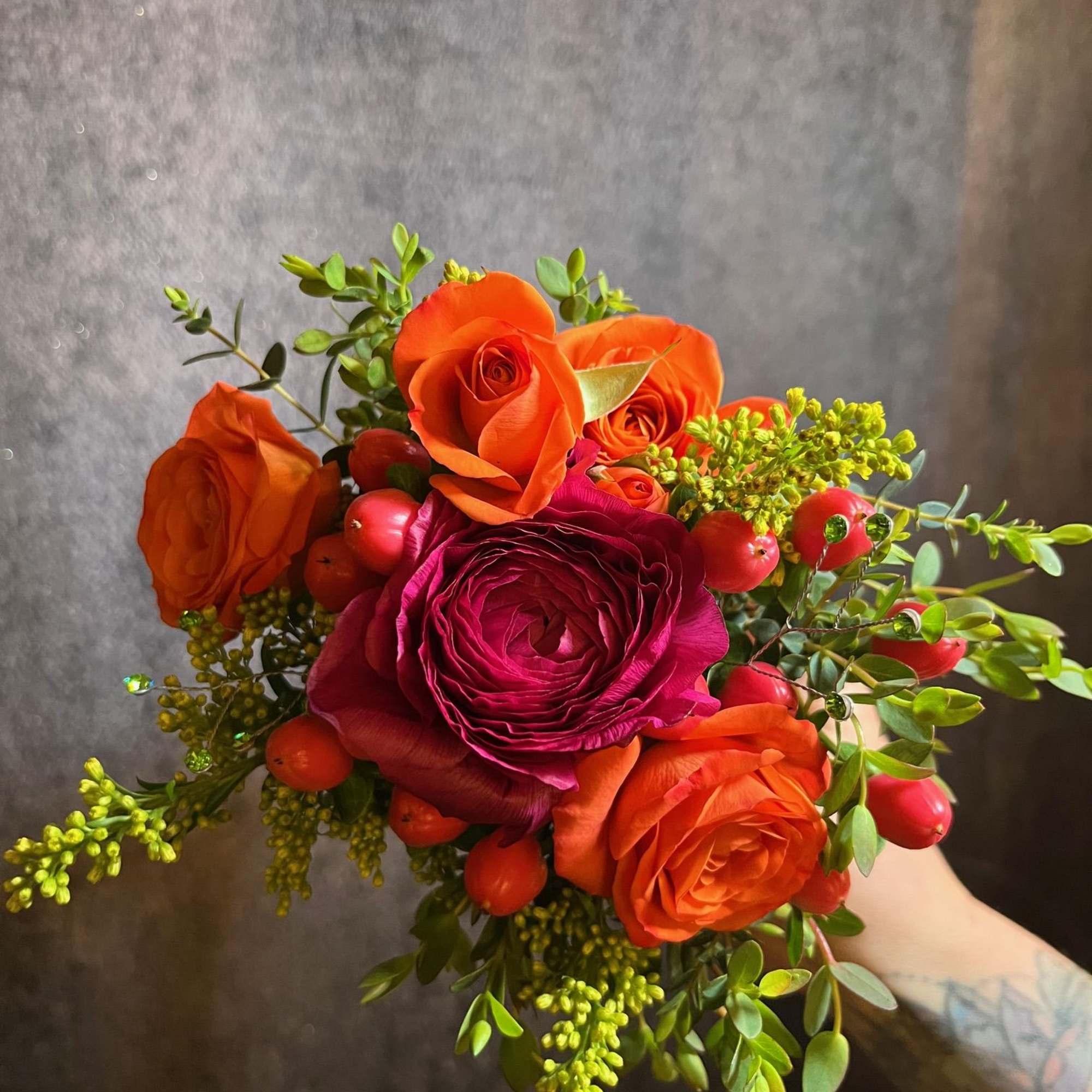 Handheld bouquet of orange and magenta roses with red berries