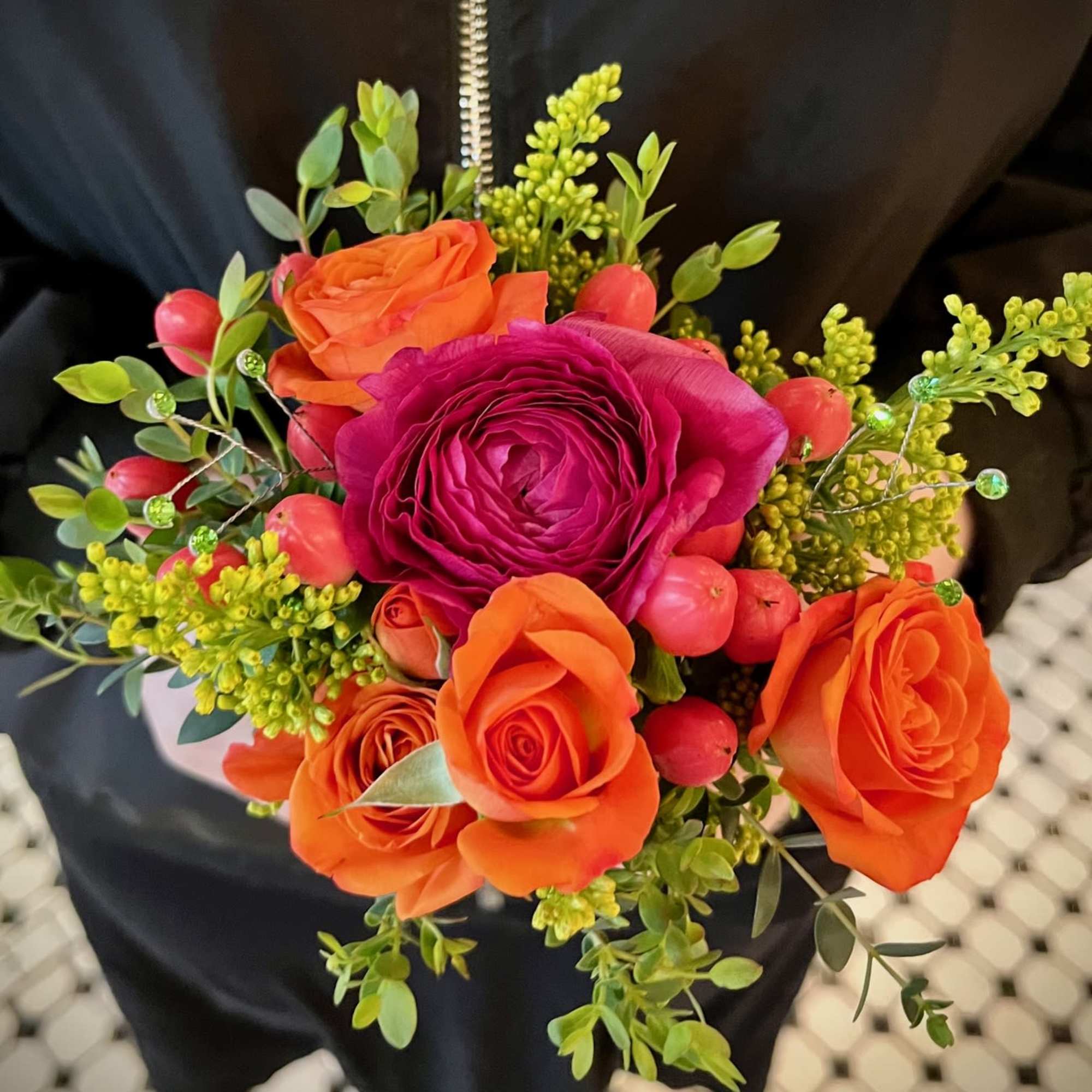 Handheld bouquet of orange and magenta roses with berry accents
