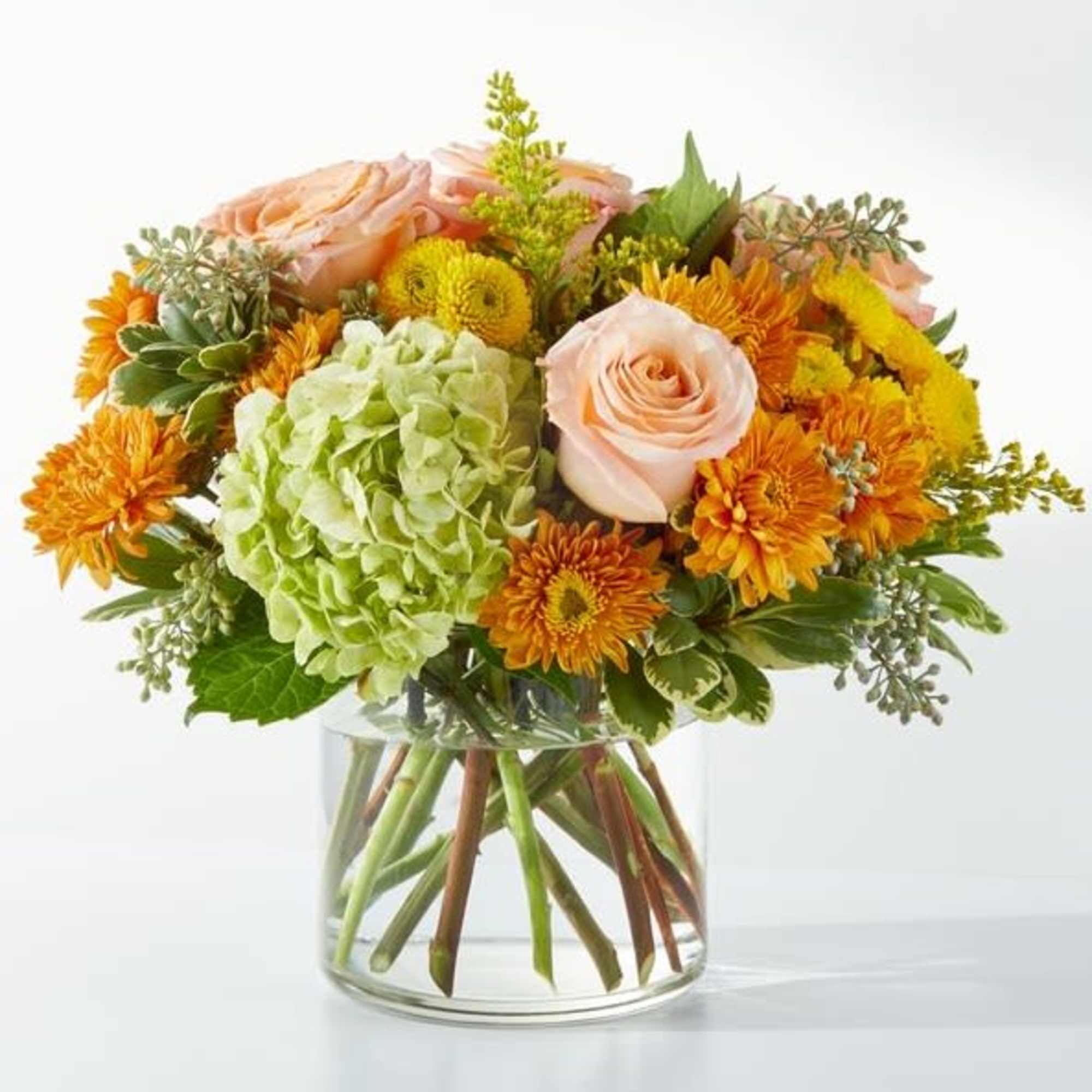 Peach roses and orange mums in a clear glass vase with green hydrangea