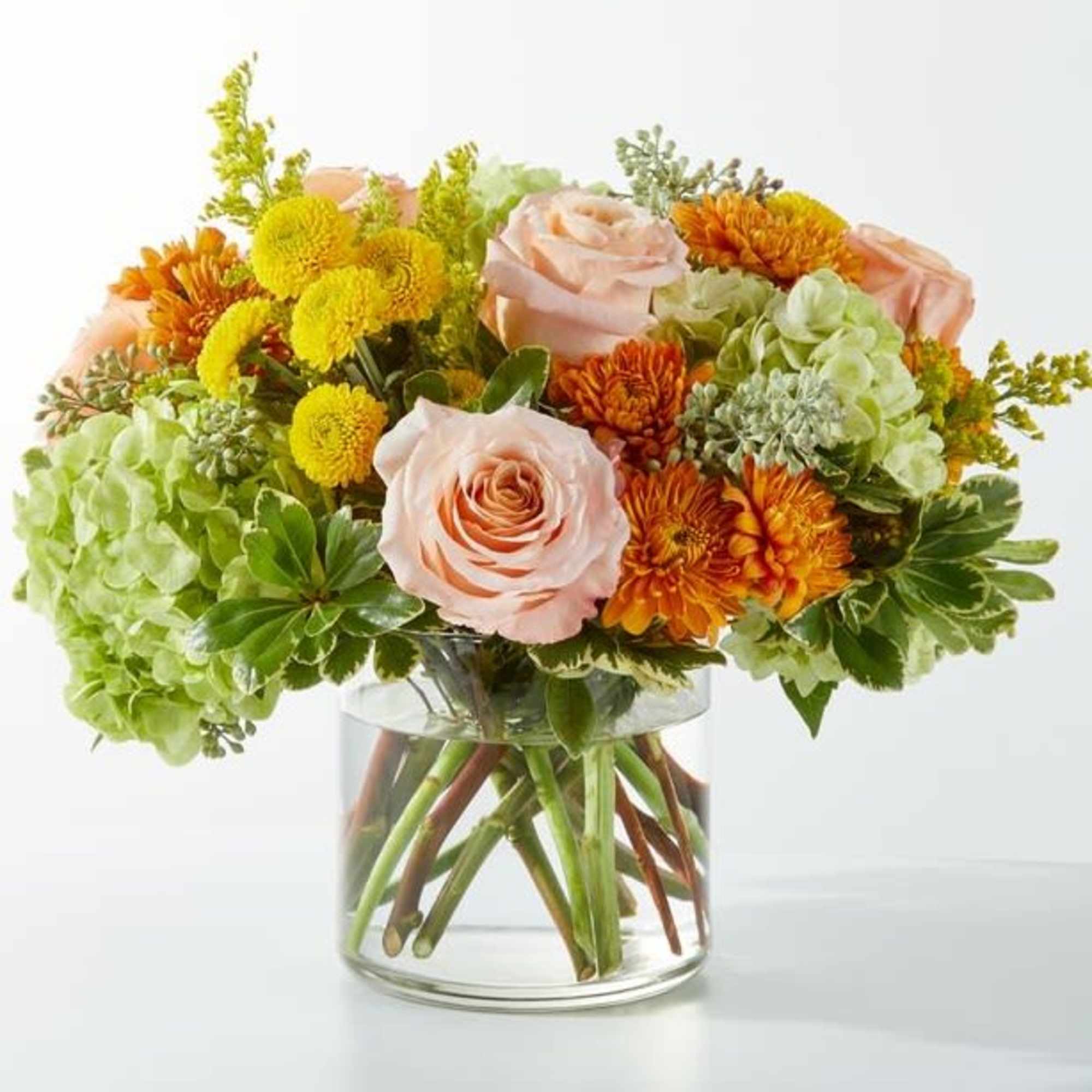 Mixed bouquet of peach roses, orange mums, and green hydrangeas in a glass vase