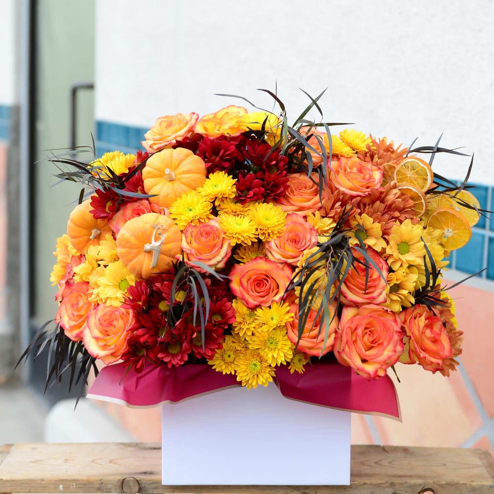 Bright mixed bouquet of roses and mums with small pumpkins in a white box