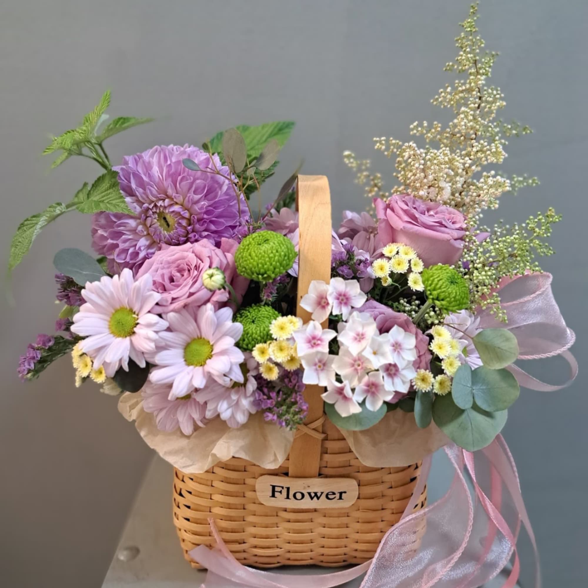 Pastel flower arrangement in a wicker basket with a ribbon handle
