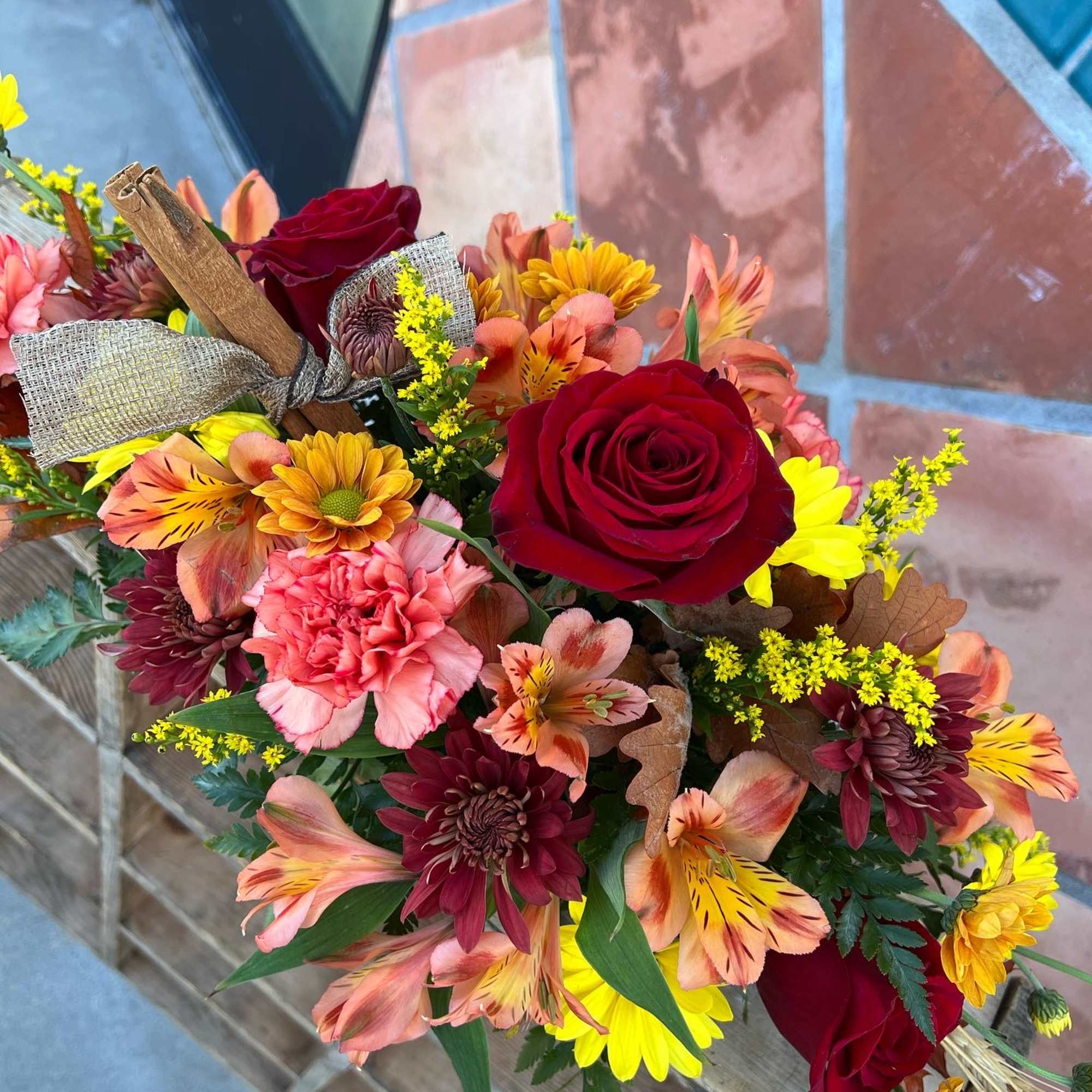 Bouquet of red roses, pink carnations, and yellow daisies with a burlap ribbon