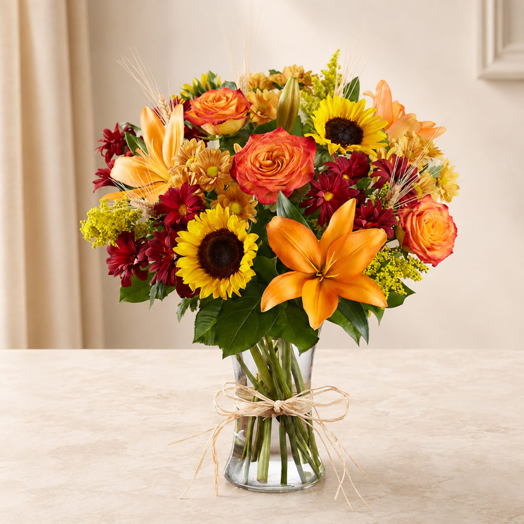 Mixed bouquet of orange roses, sunflowers, lilies, and daisies in a glass vase