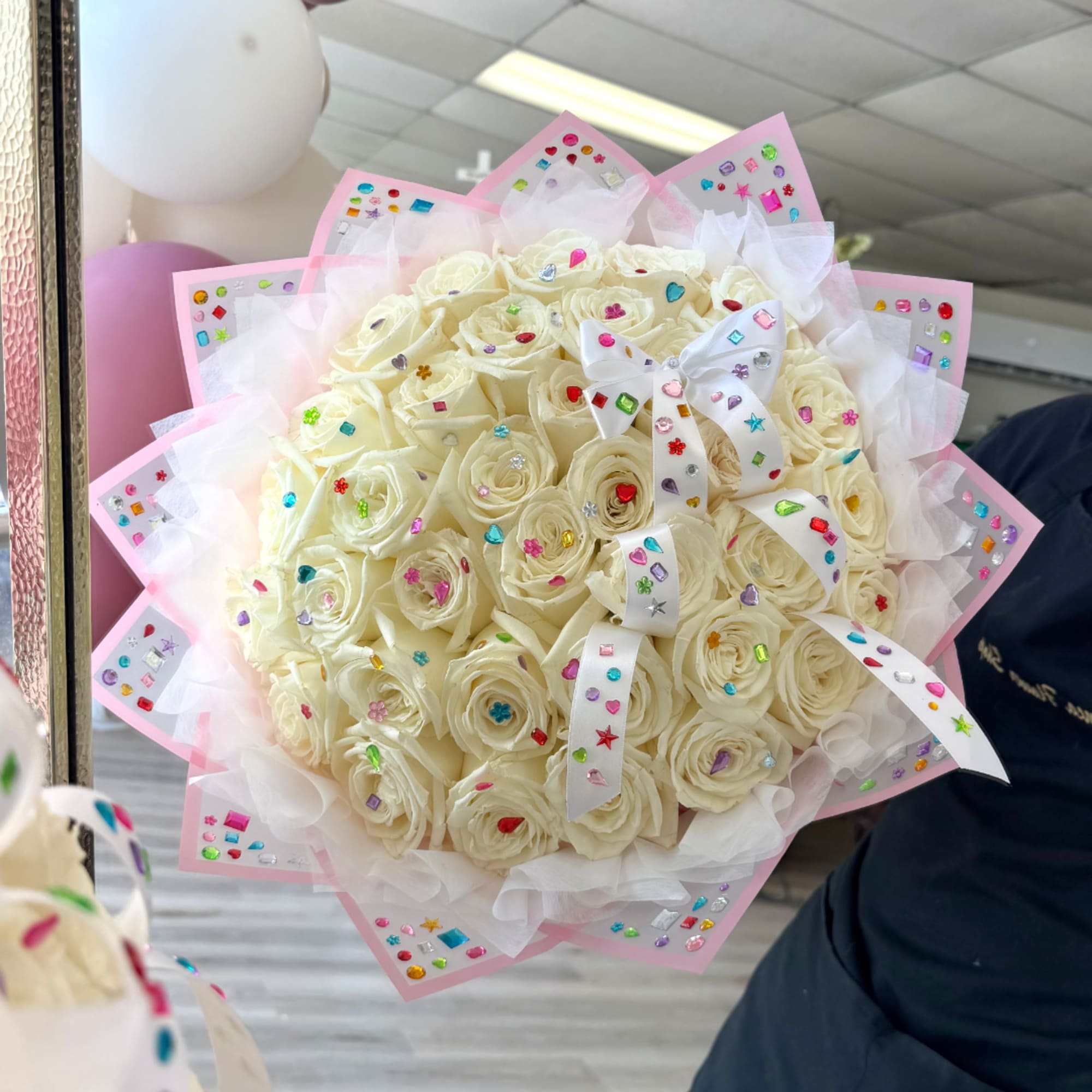 Bouquet of cream roses wrapped in pink paper with jeweled ribbon accents