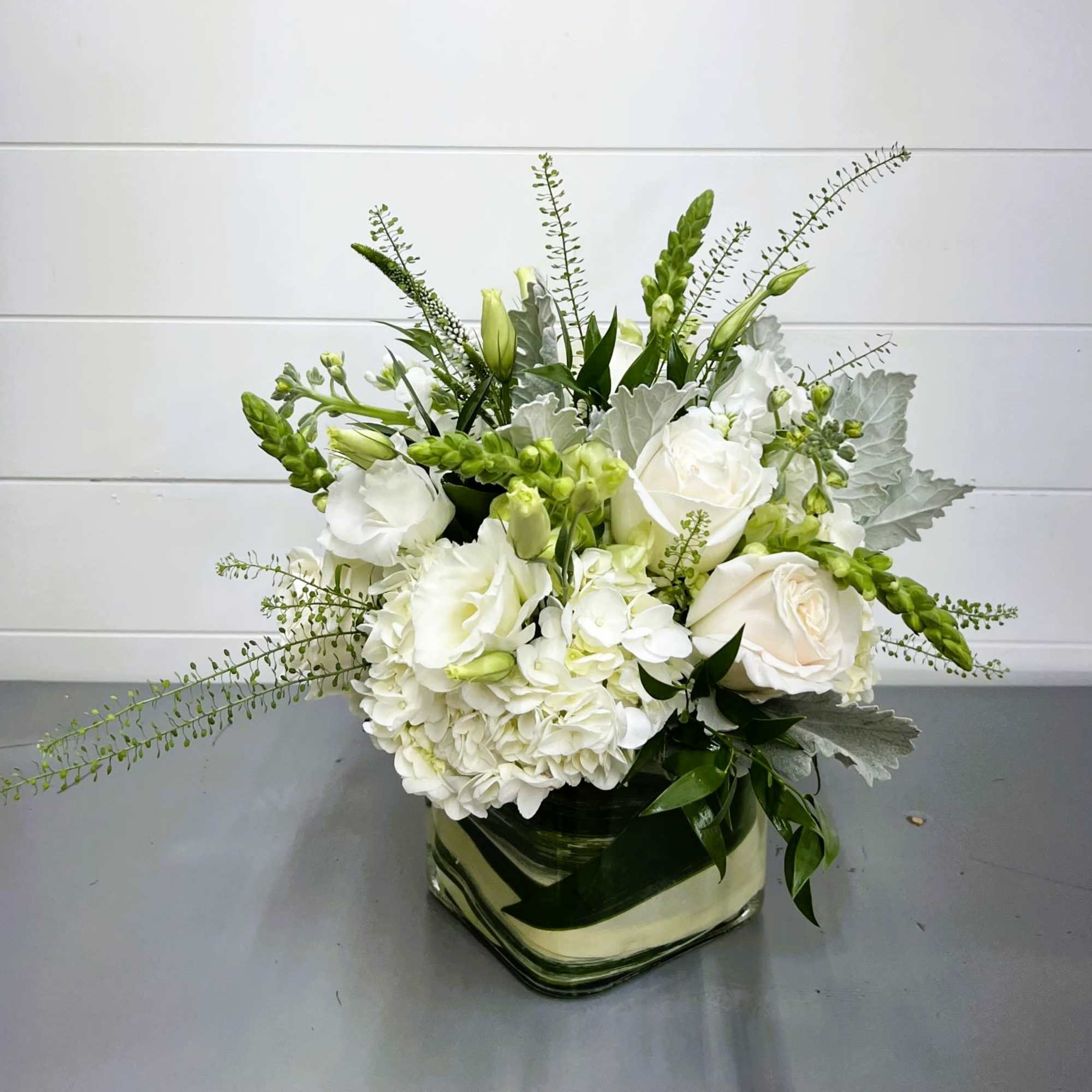 White floral arrangement in a square glass vase with green accents