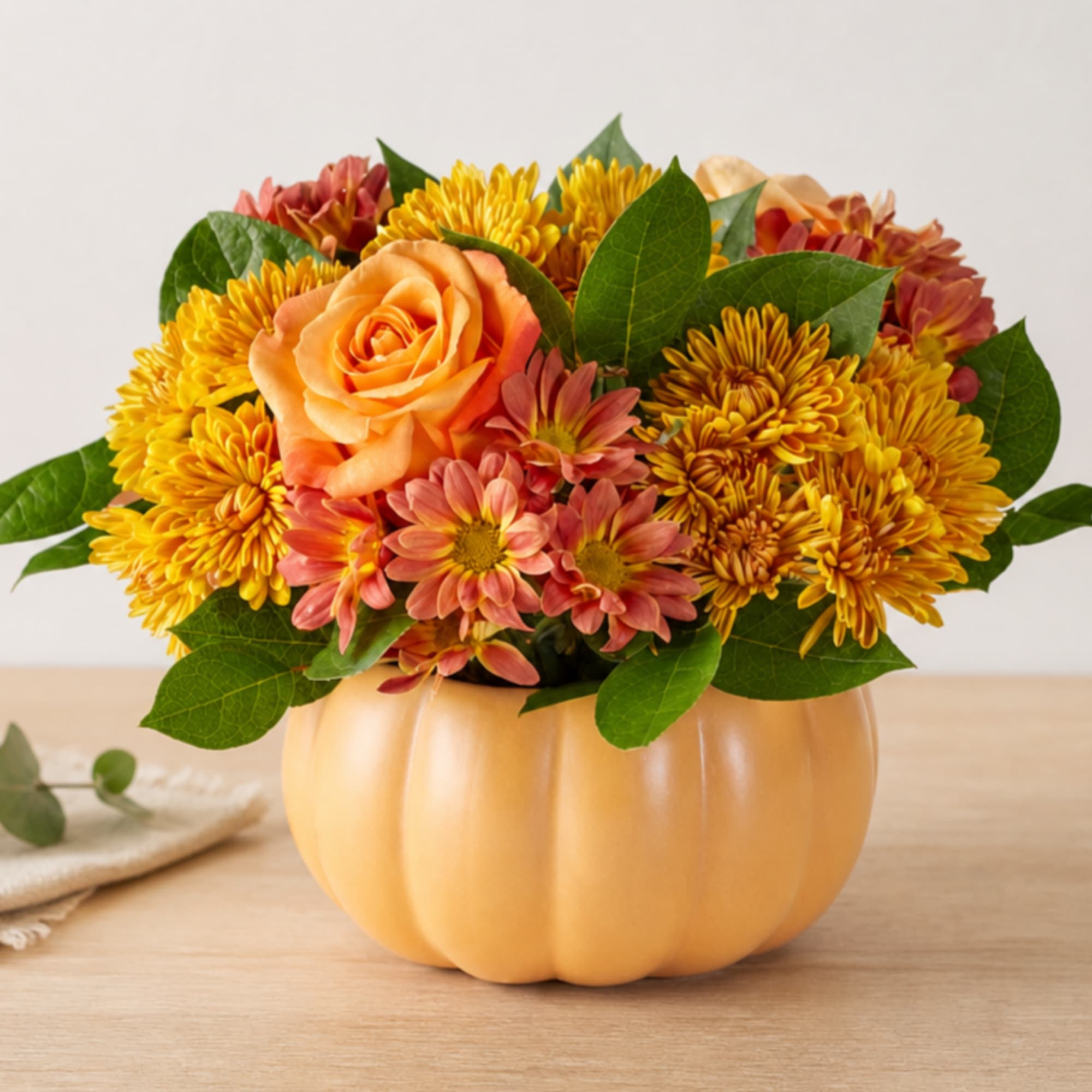 Orange rose and yellow chrysanthemum arrangement in a pumpkin-shaped container