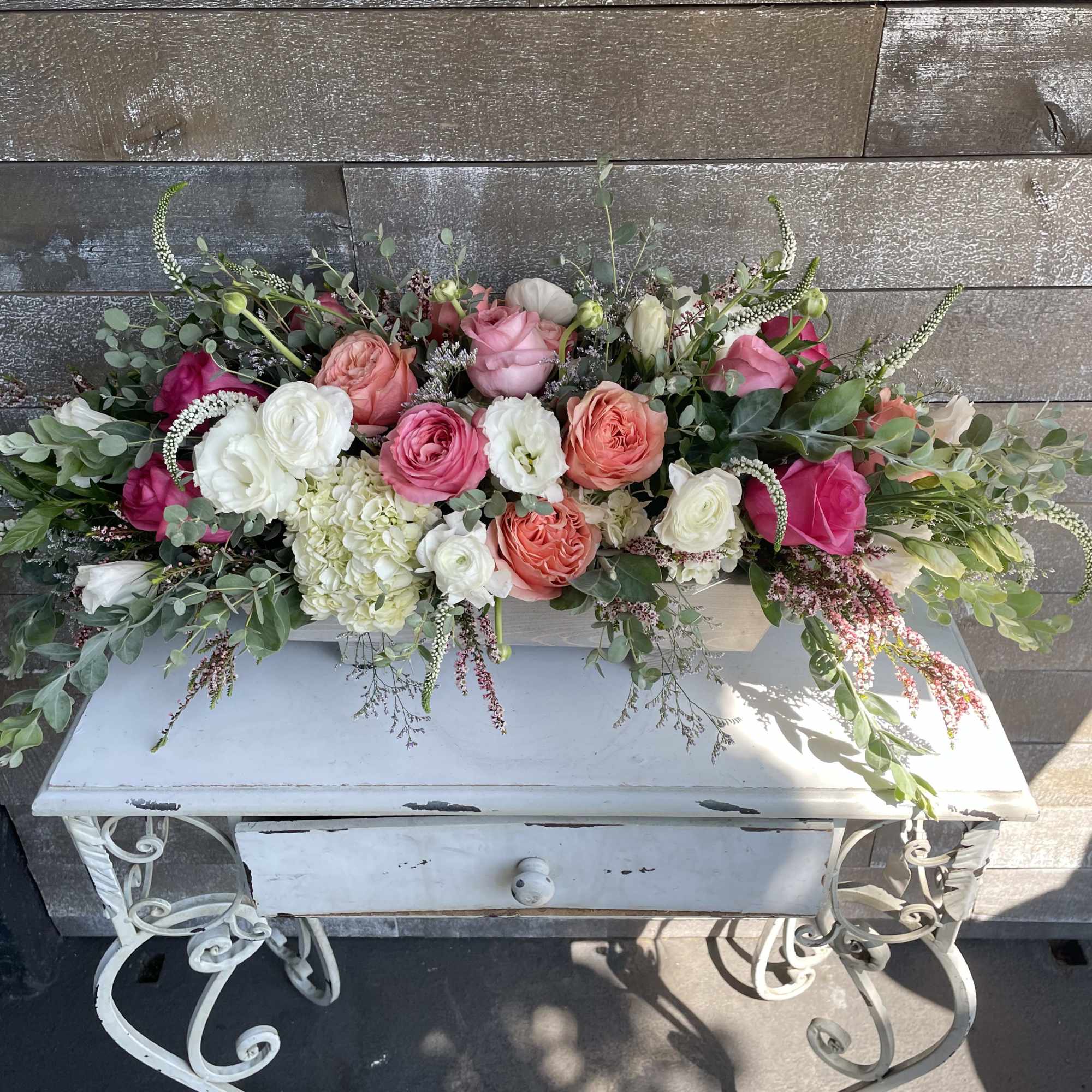 Long low arrangement of pink, peach, and white roses in a white container