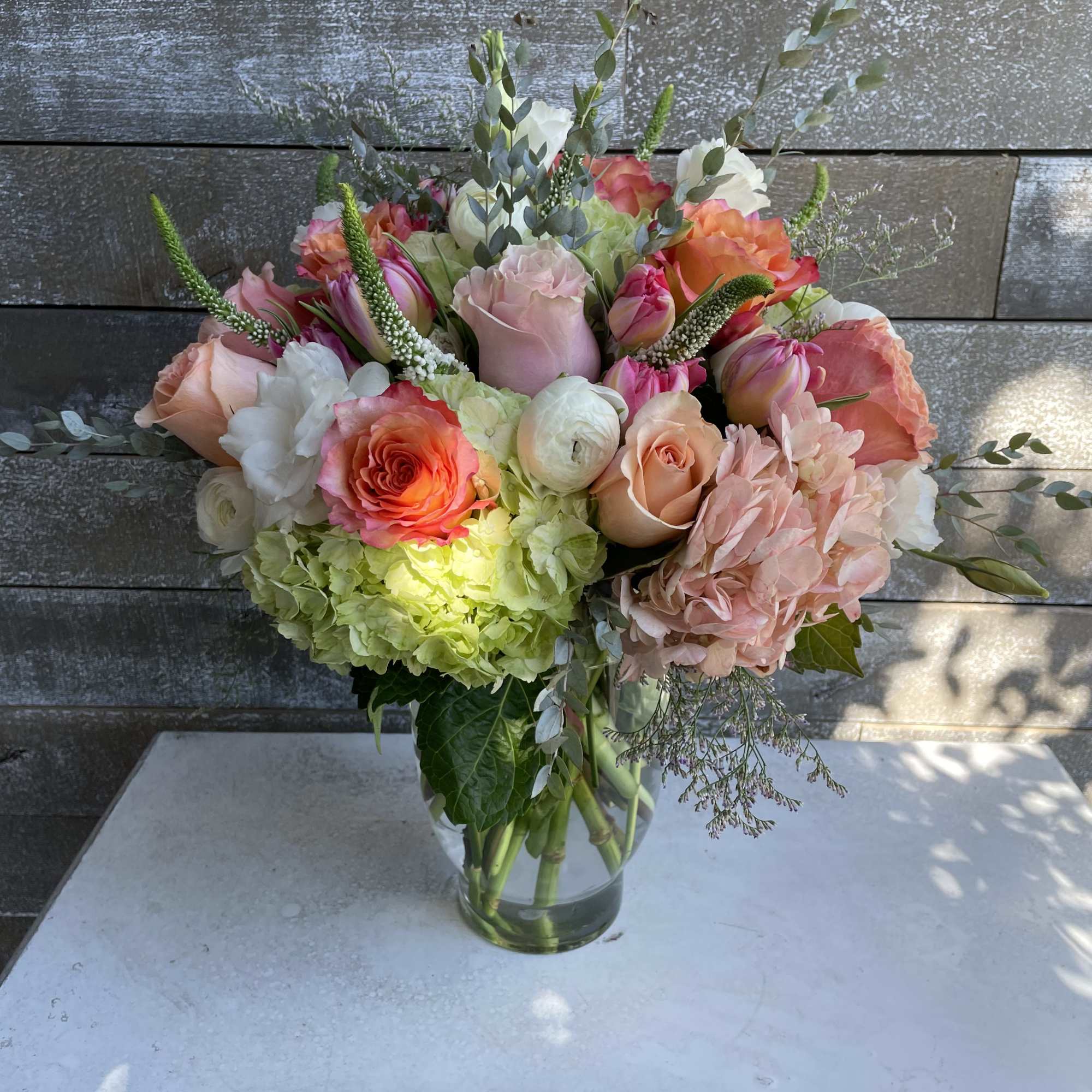 Mixed bouquet of pink, peach, white, and green flowers in a glass vase