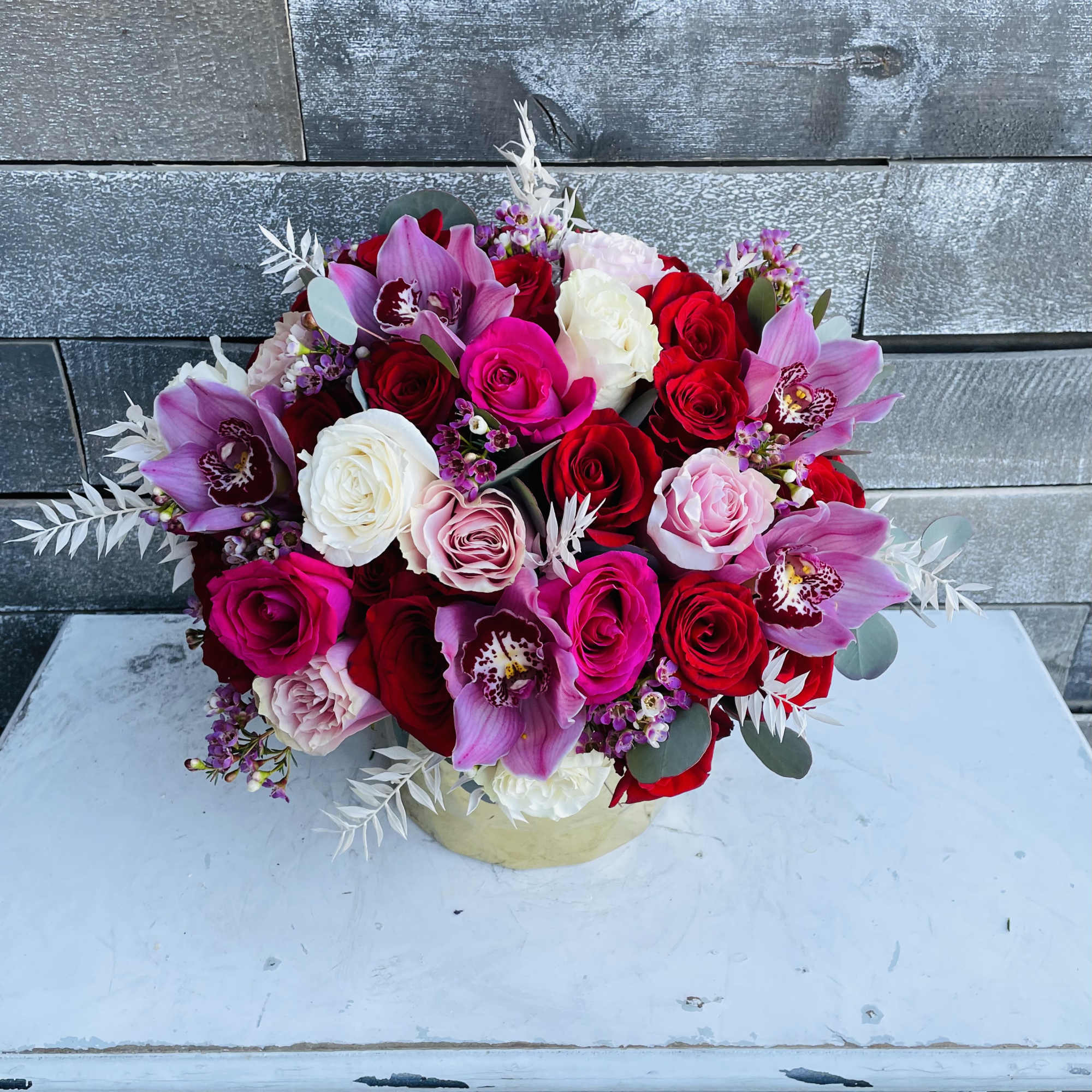 Bouquet of red, pink, and white roses with purple orchids in a round box