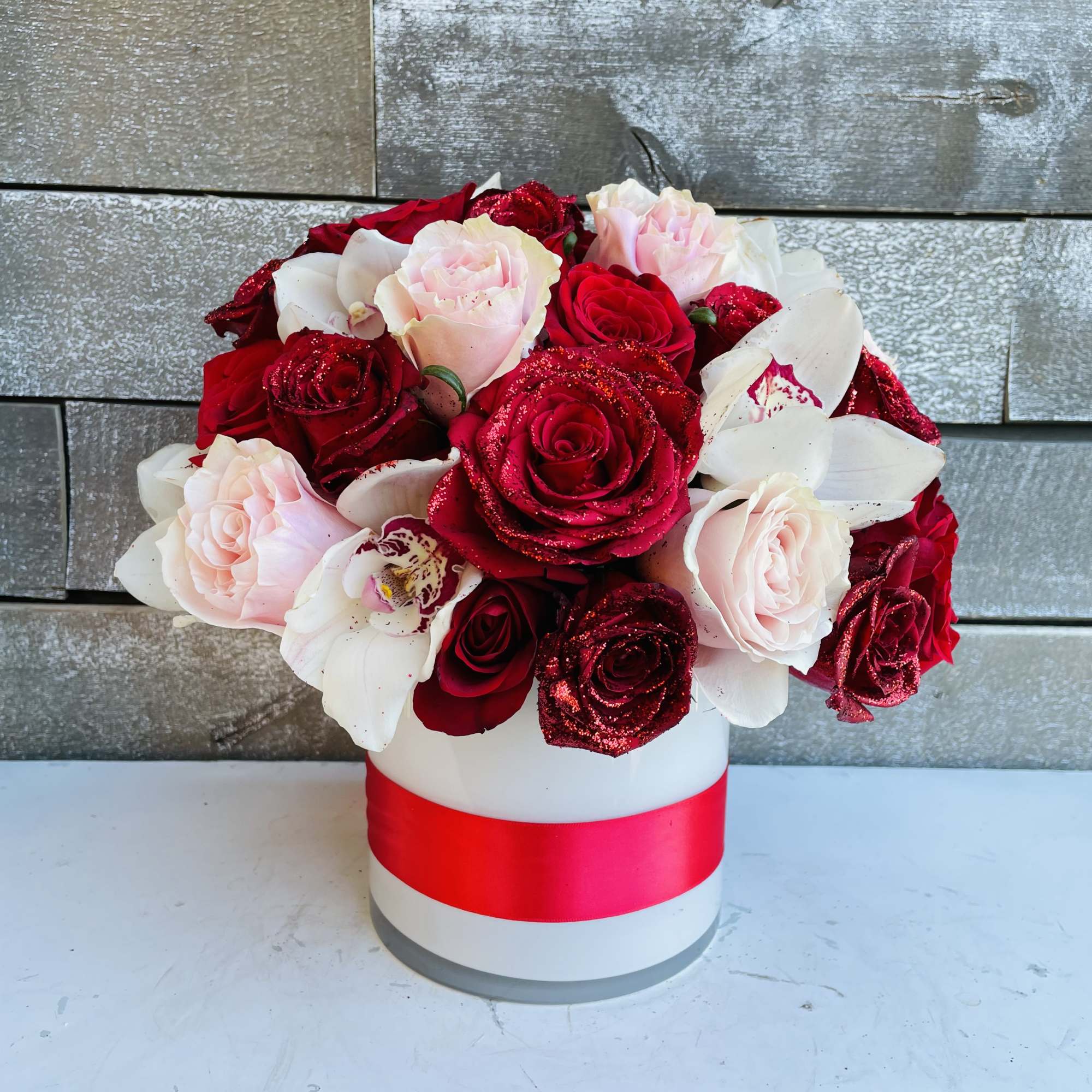 Red and white roses arranged in a white hat box with a red ribbon
