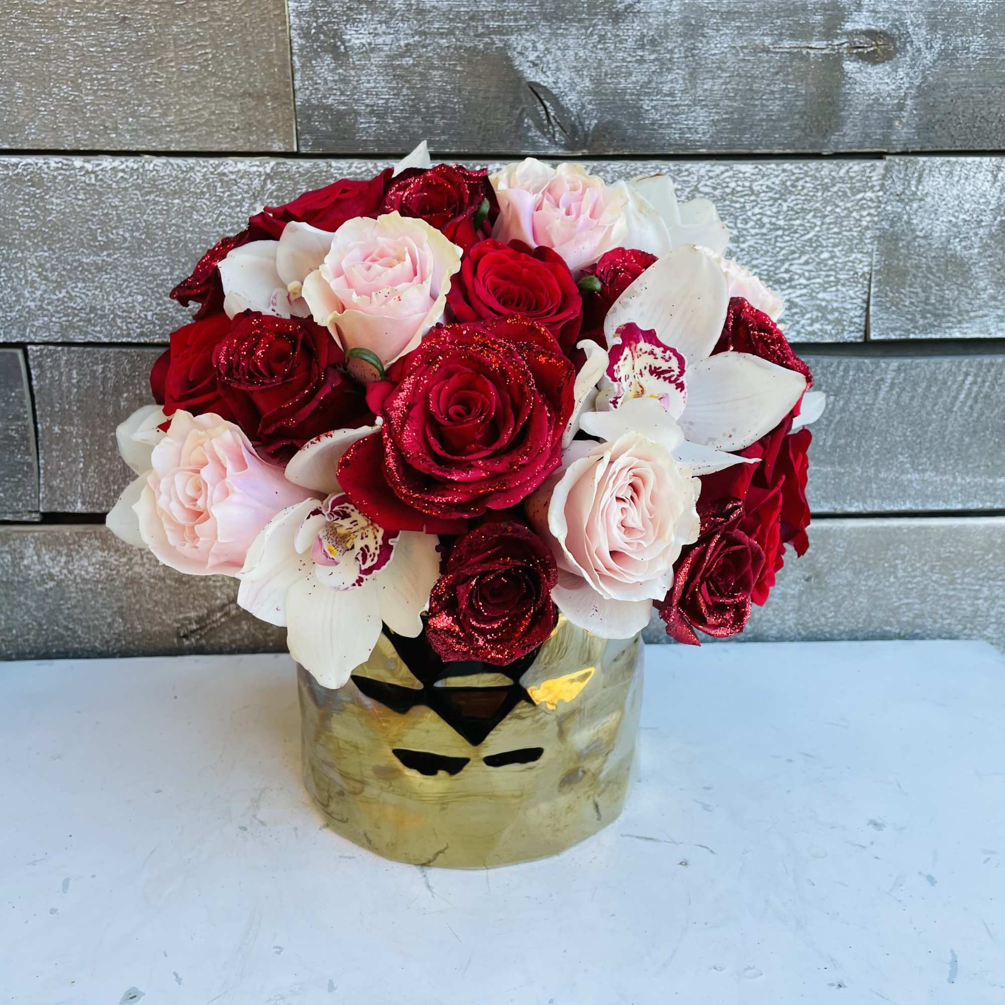 Bouquet of red and pale pink roses with white orchids in a gold vase