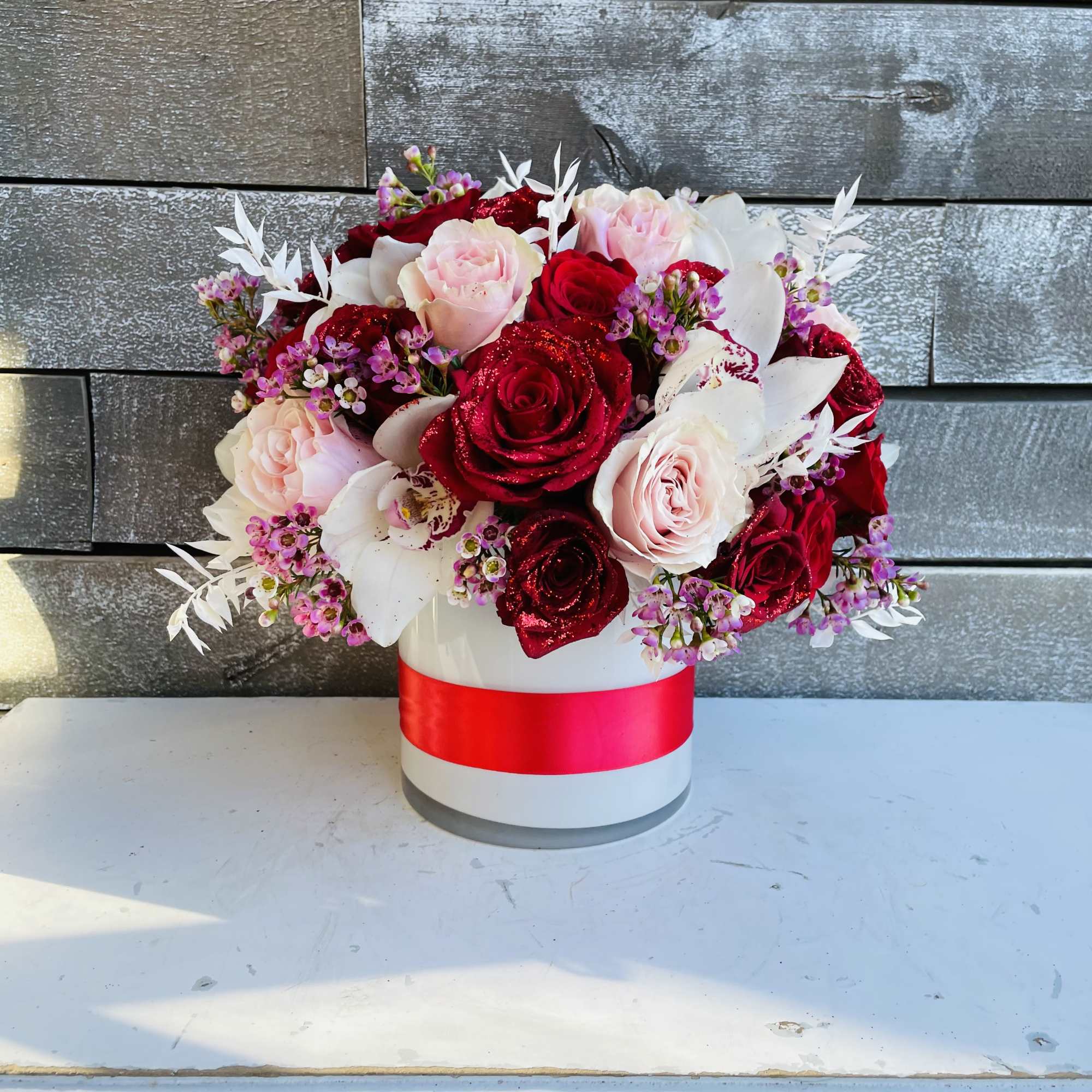 Red and blush roses arranged in a white hatbox with a pink ribbon