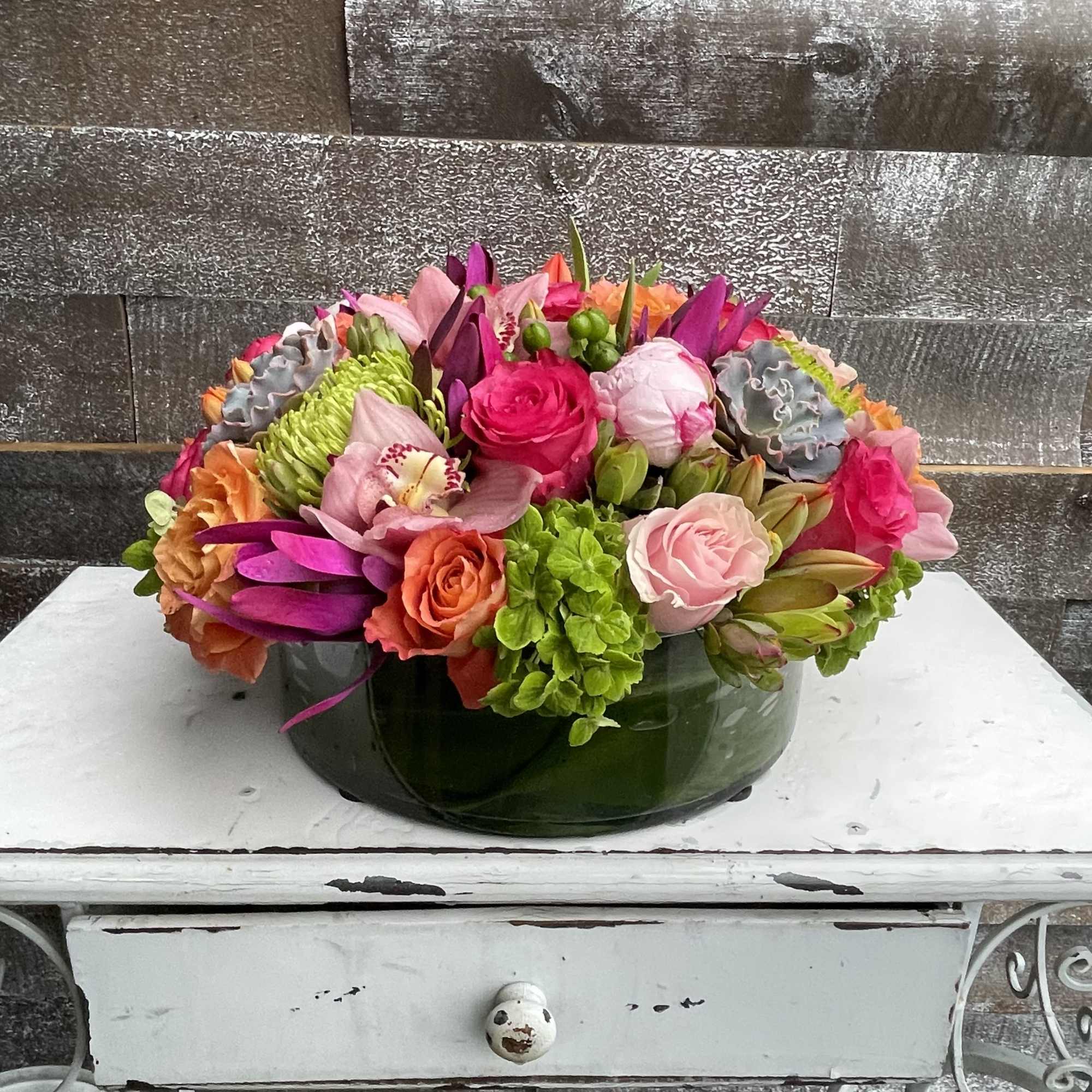 Colorful mixed flower arrangement in a low green glass bowl