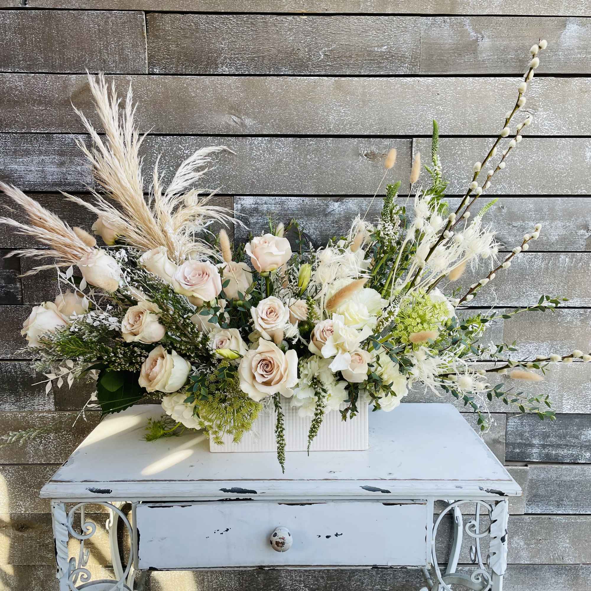 Large floral arrangement with pale roses and dried grasses in a white container