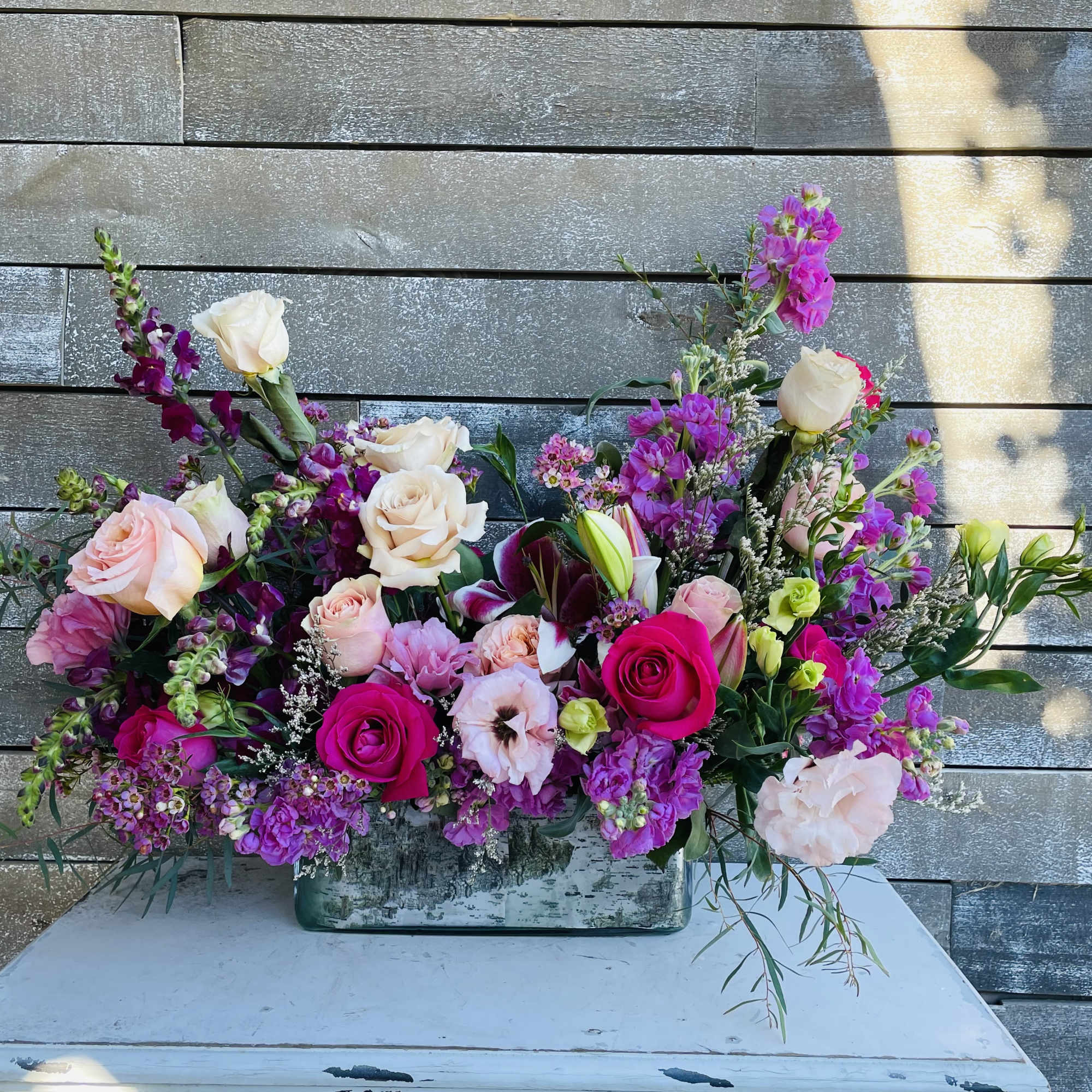 Mixed bouquet of pink and cream roses with purple blooms in a rectangular vase