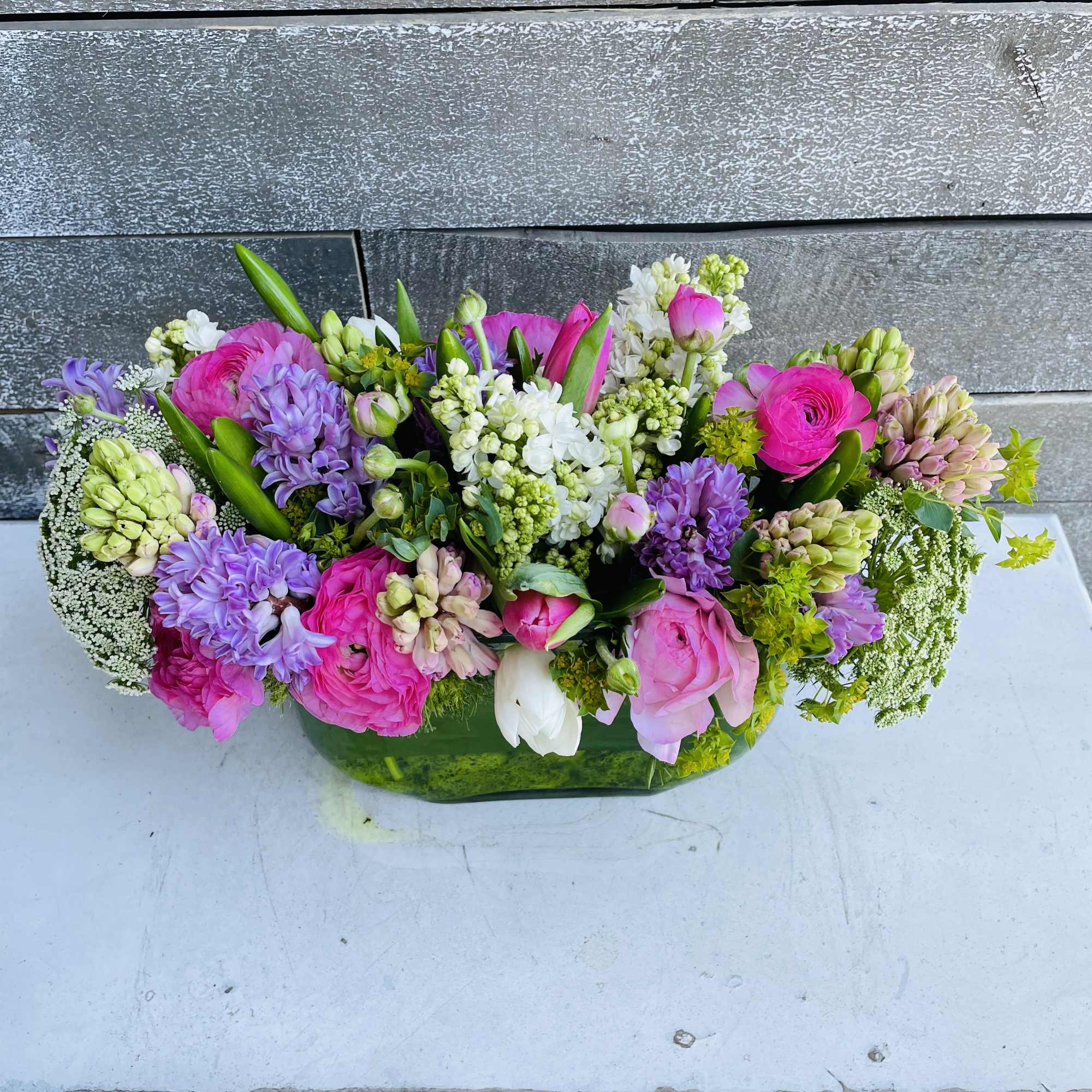 Mixed pink, purple, and white flowers arranged in a low green container