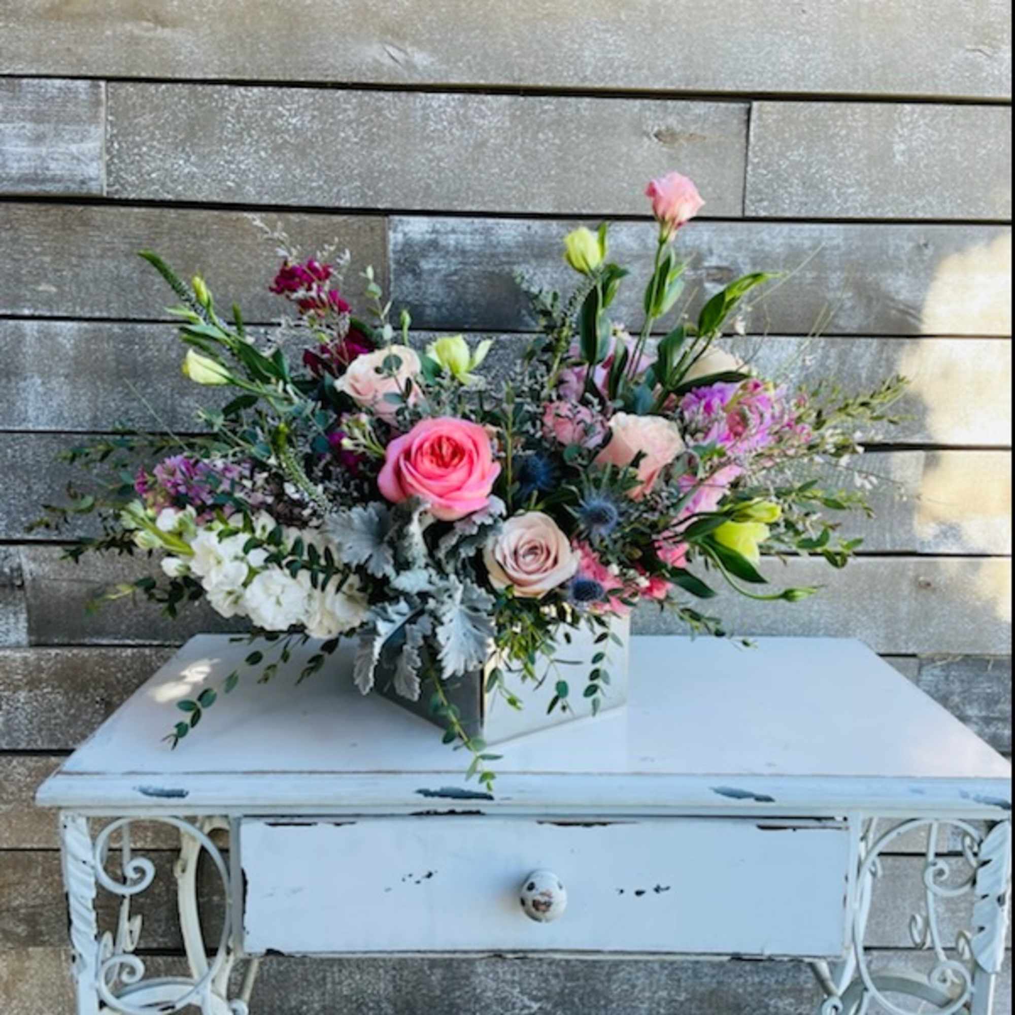 Mixed pink and white floral arrangement in a white container on a table