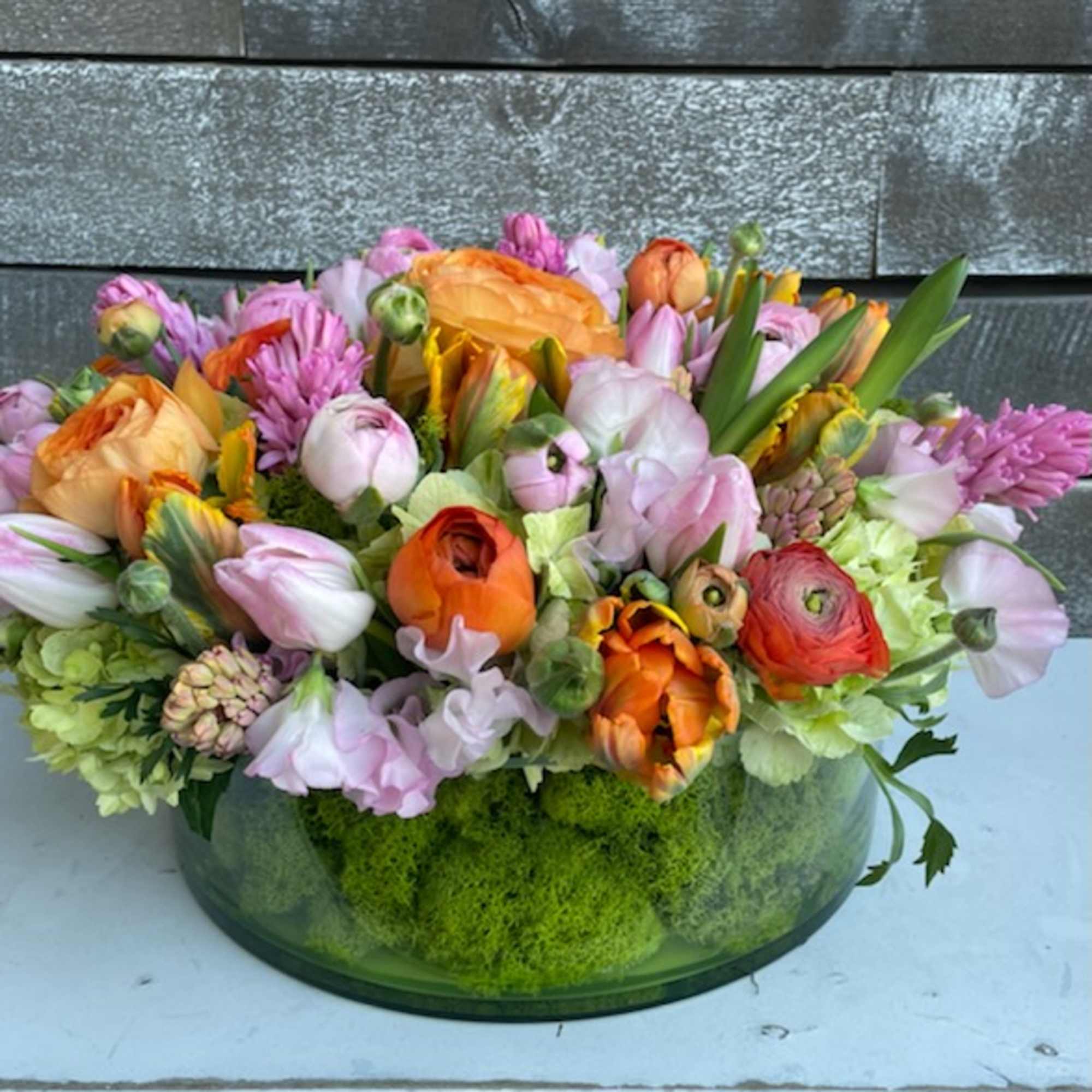 Mixed bouquet of orange, pink, and lavender flowers in a low glass bowl