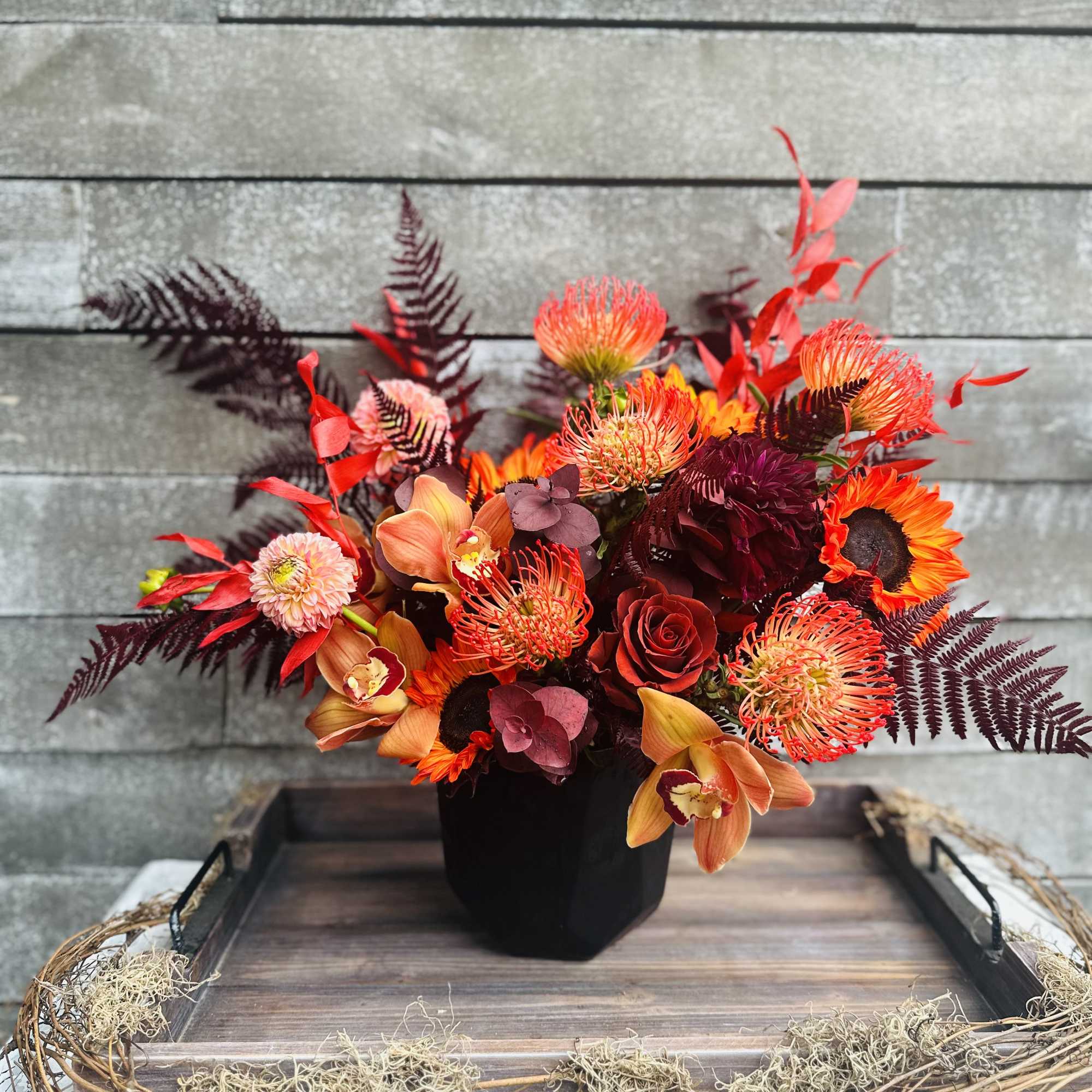 Orange and burgundy floral arrangement in a black vase
