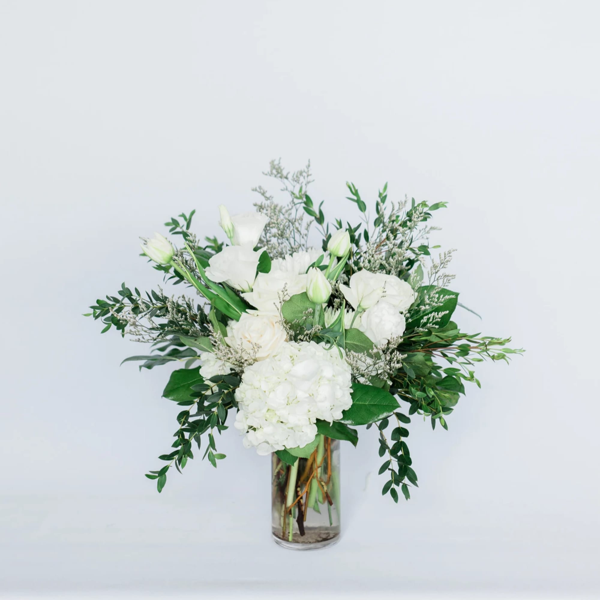 White floral arrangement in a clear glass vase with greenery