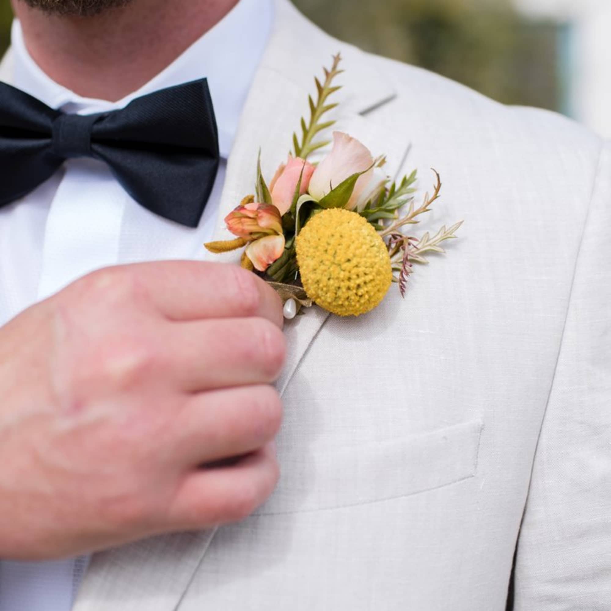 Boutonniere with yellow and blush flowers on a white suit jacket