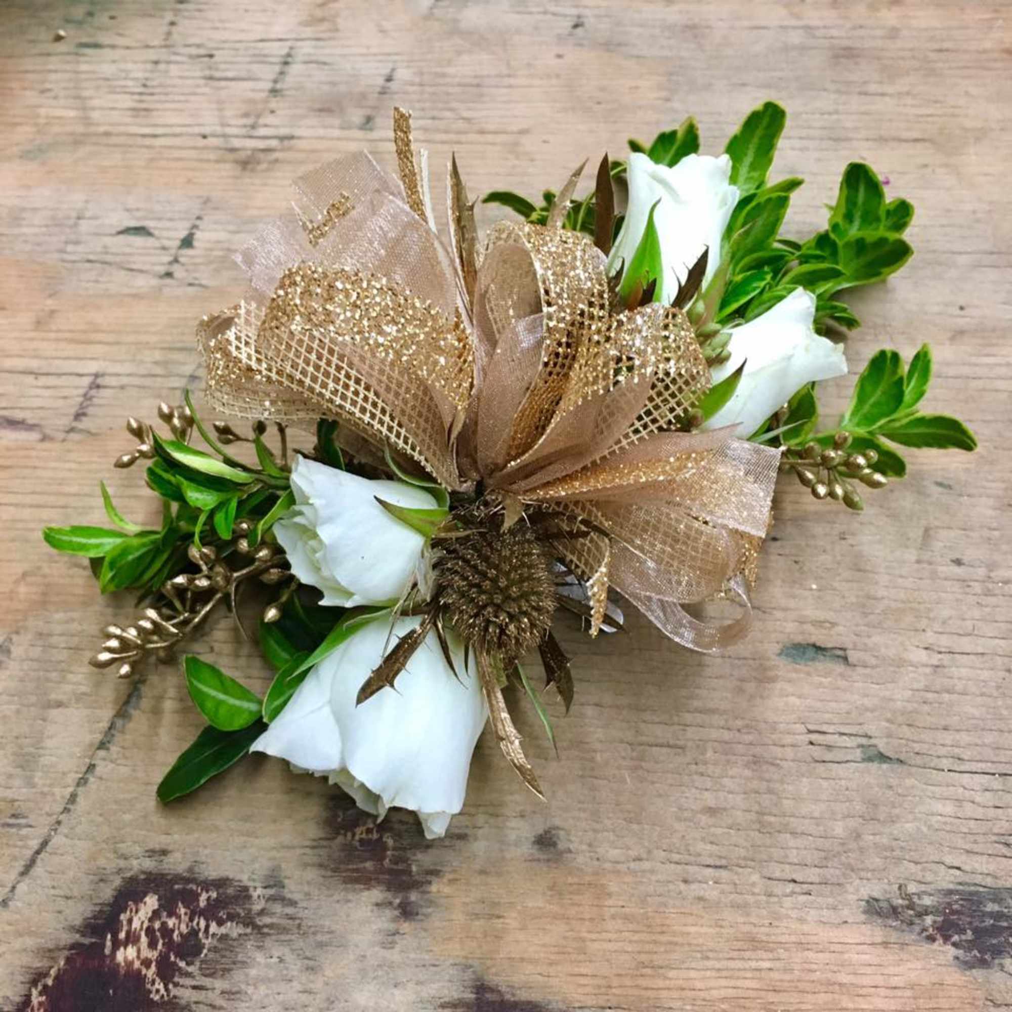 White rose corsage with gold ribbon and greenery on a wooden surface