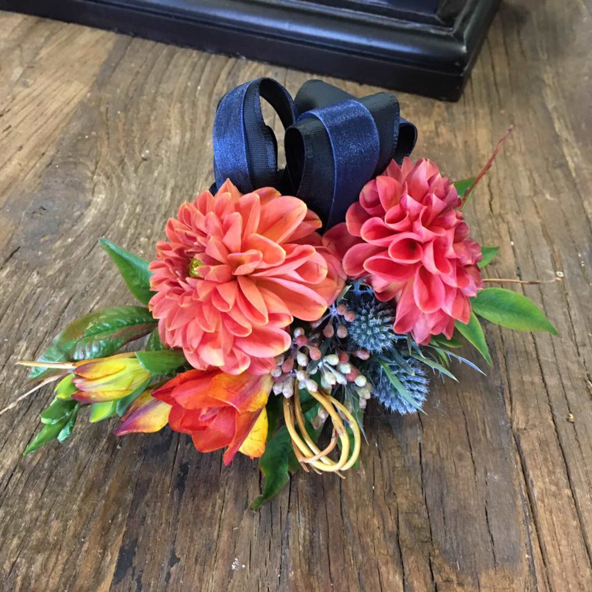 Small floral arrangement with pink and orange blooms and a navy ribbon bow