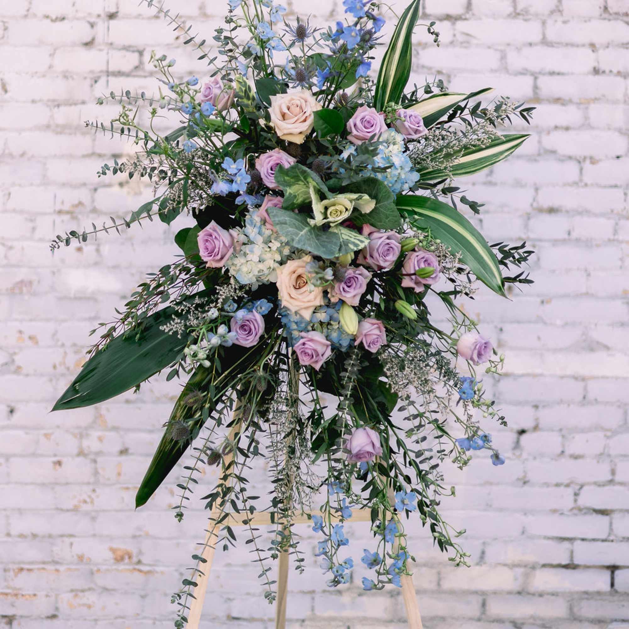 Tall floral spray with lavender and blue flowers on an easel
