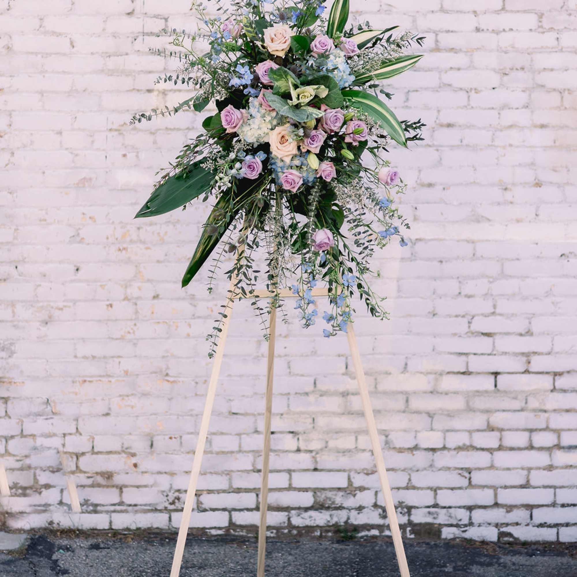 Tall floral spray on a wooden easel with pastel roses and blue flowers