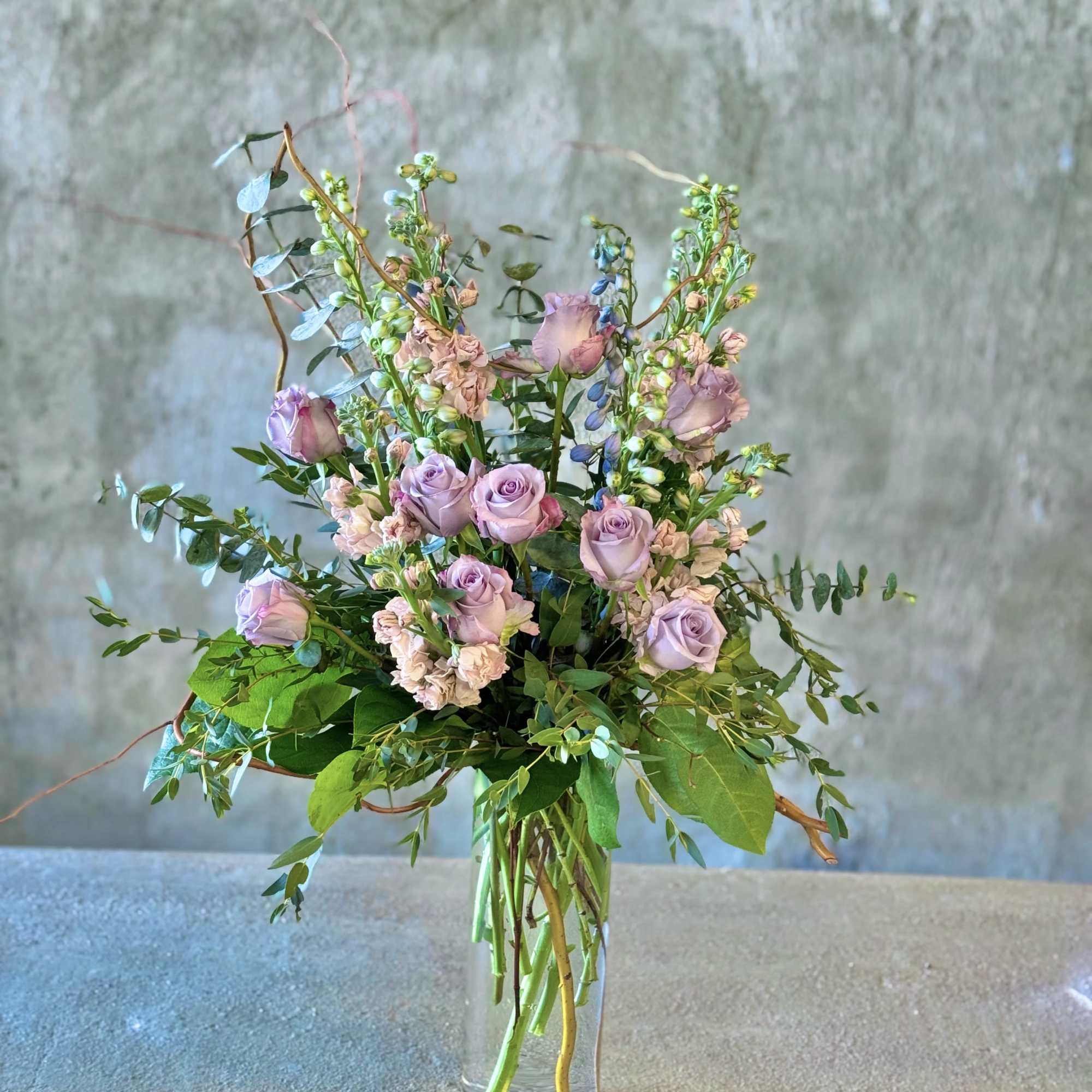 Lavender roses and mixed greenery in a clear glass vase