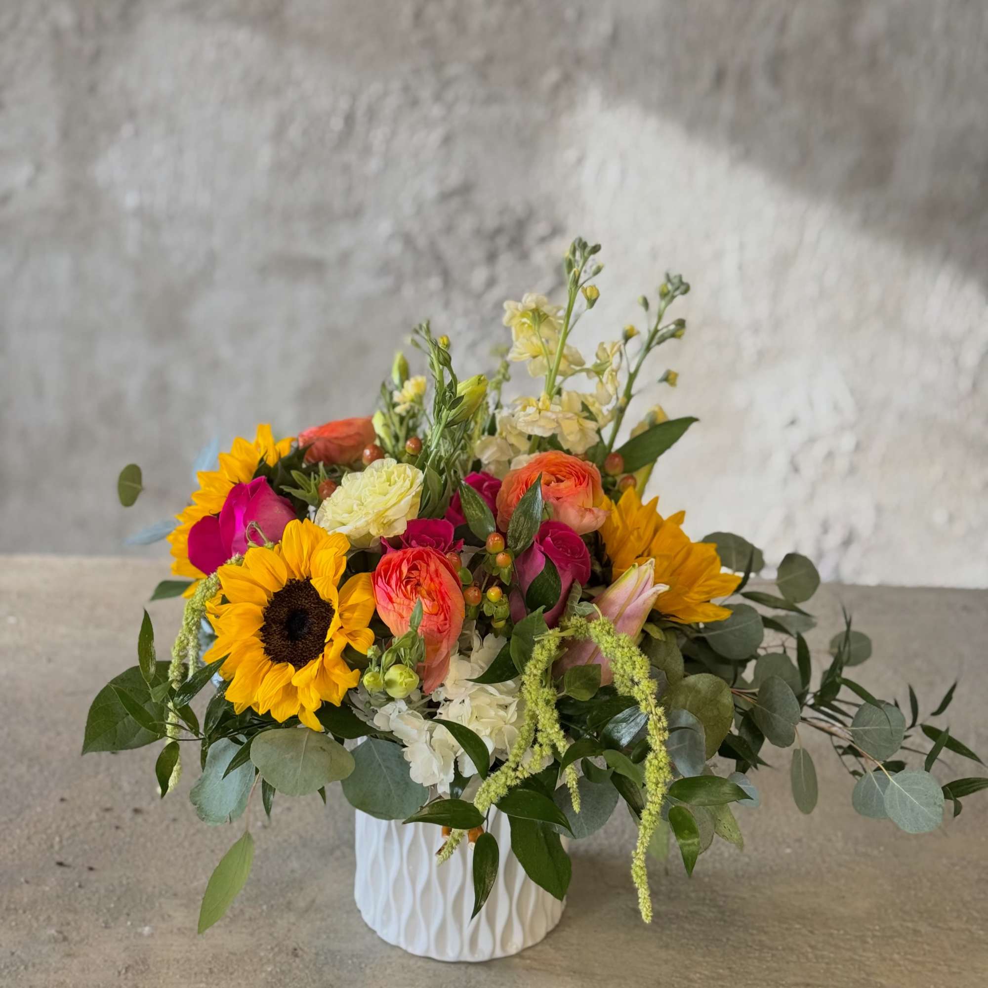 Mixed bouquet in a white textured vase with sunflowers and bright pink blooms