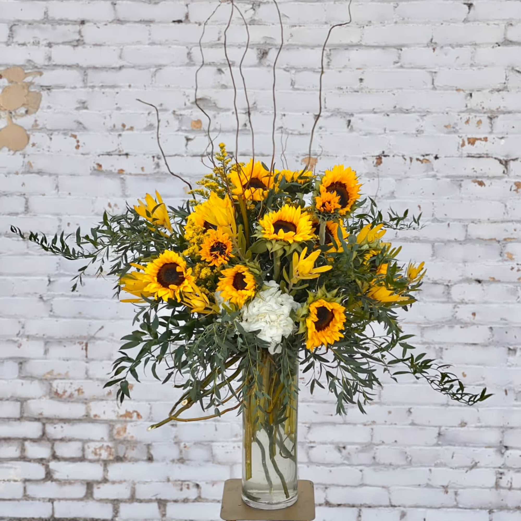 Tall sunflower arrangement in a clear glass vase with white blooms and branches