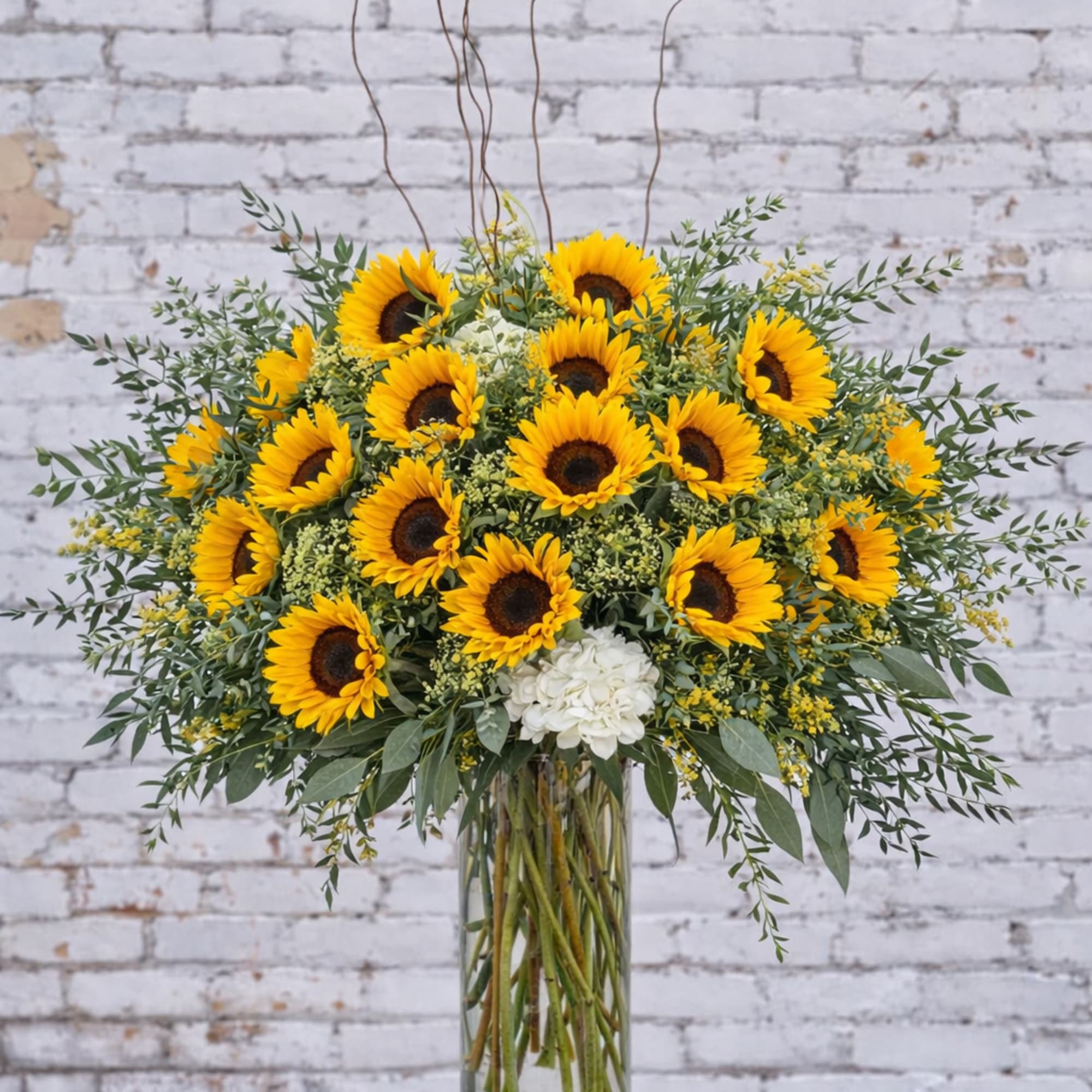Sunflower arrangement in a clear glass vase with white accent flowers