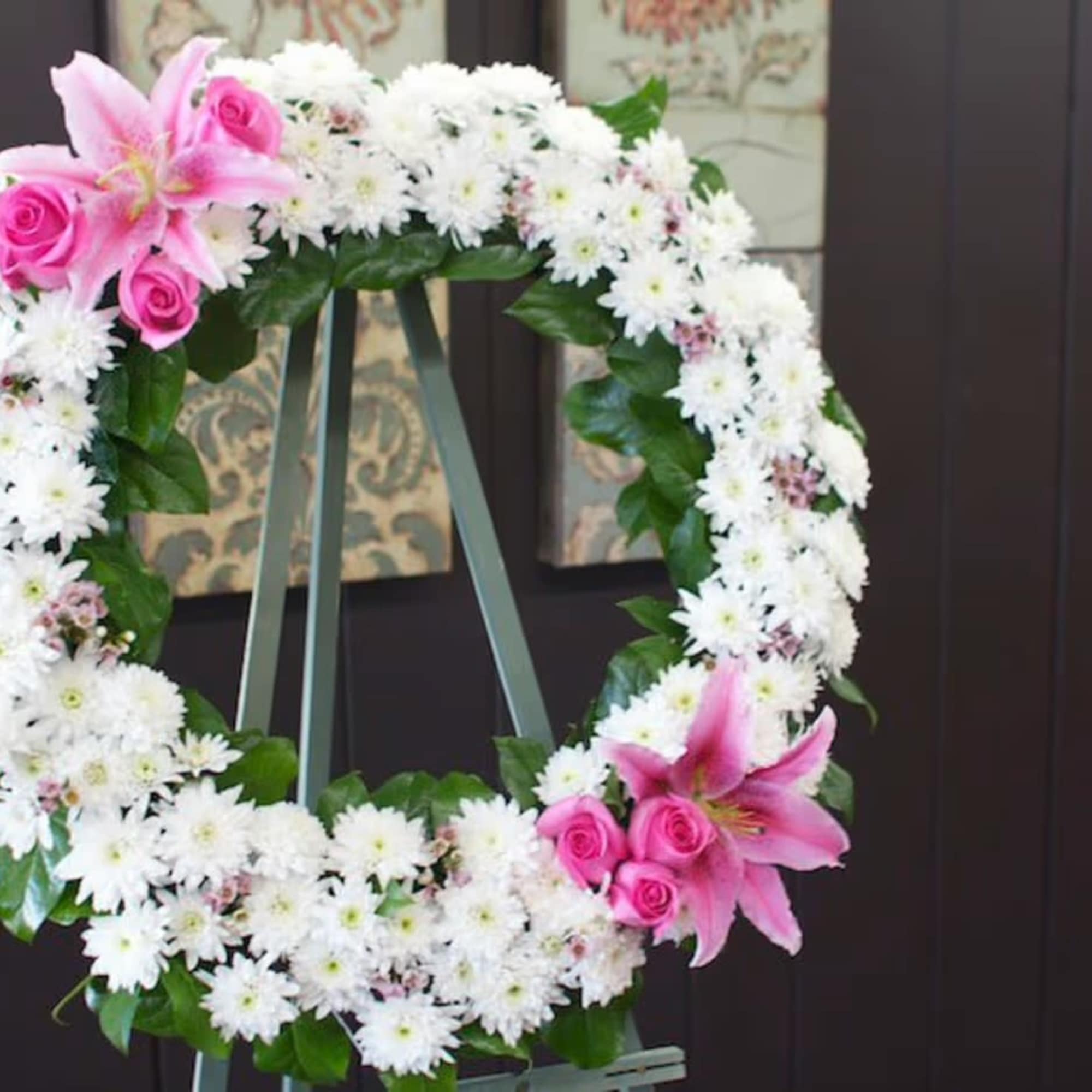 Pink lilies and roses on a white floral wreath on an easel