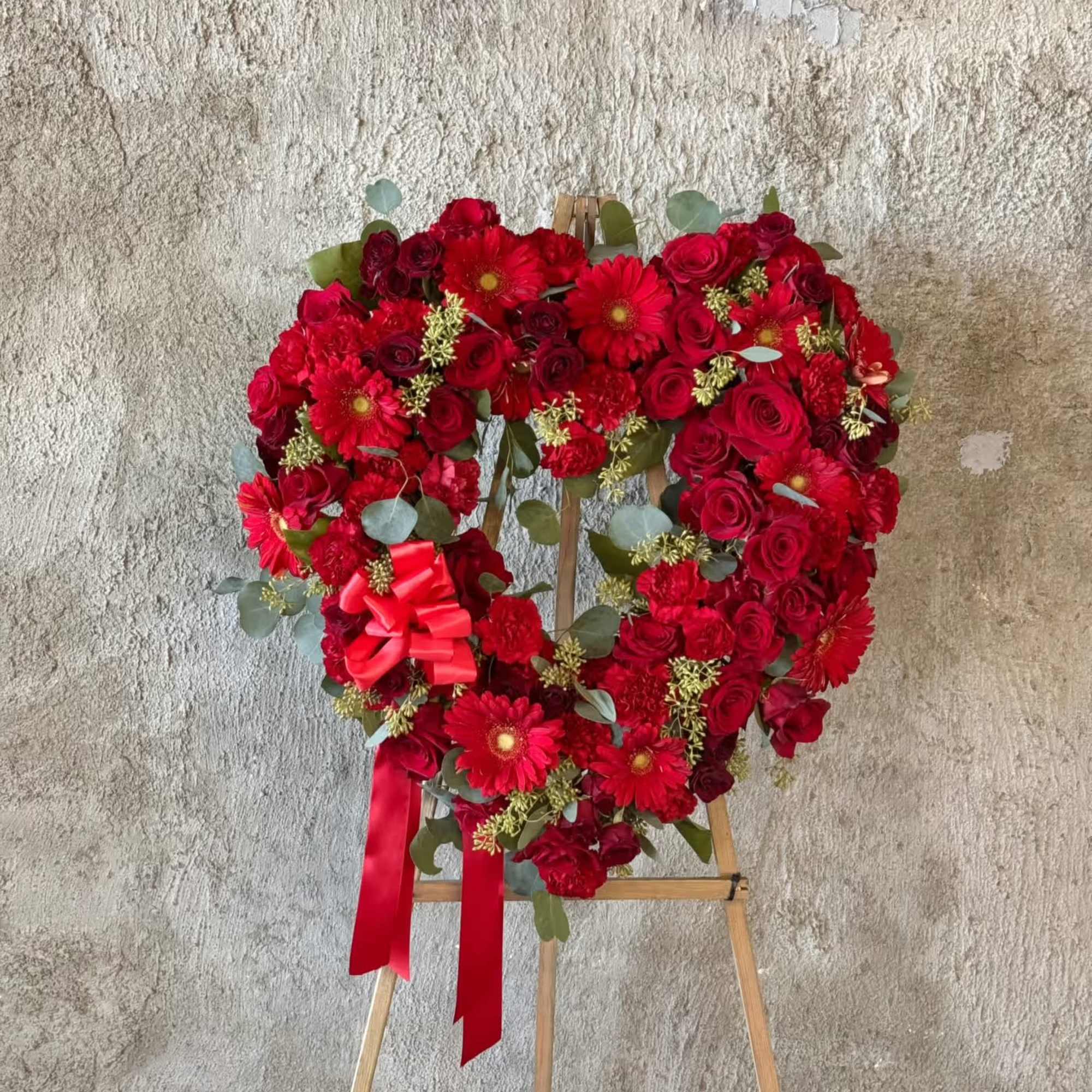 Heart-shaped red floral wreath on an easel with ribbon