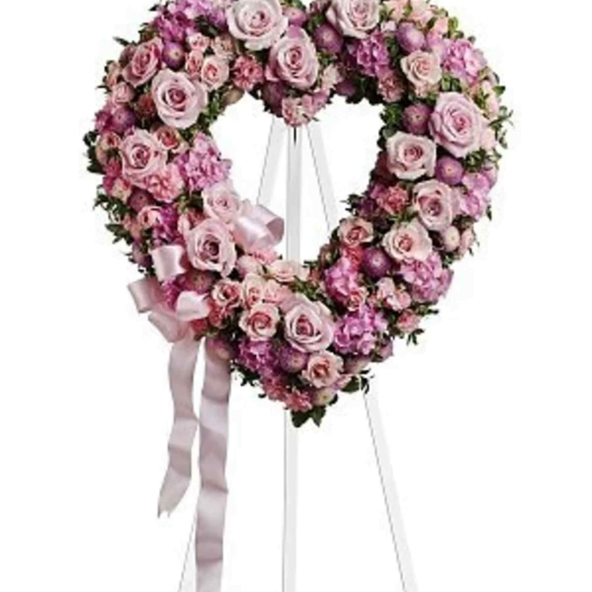 Heart-shaped pink floral wreath on a white stand with ribbon