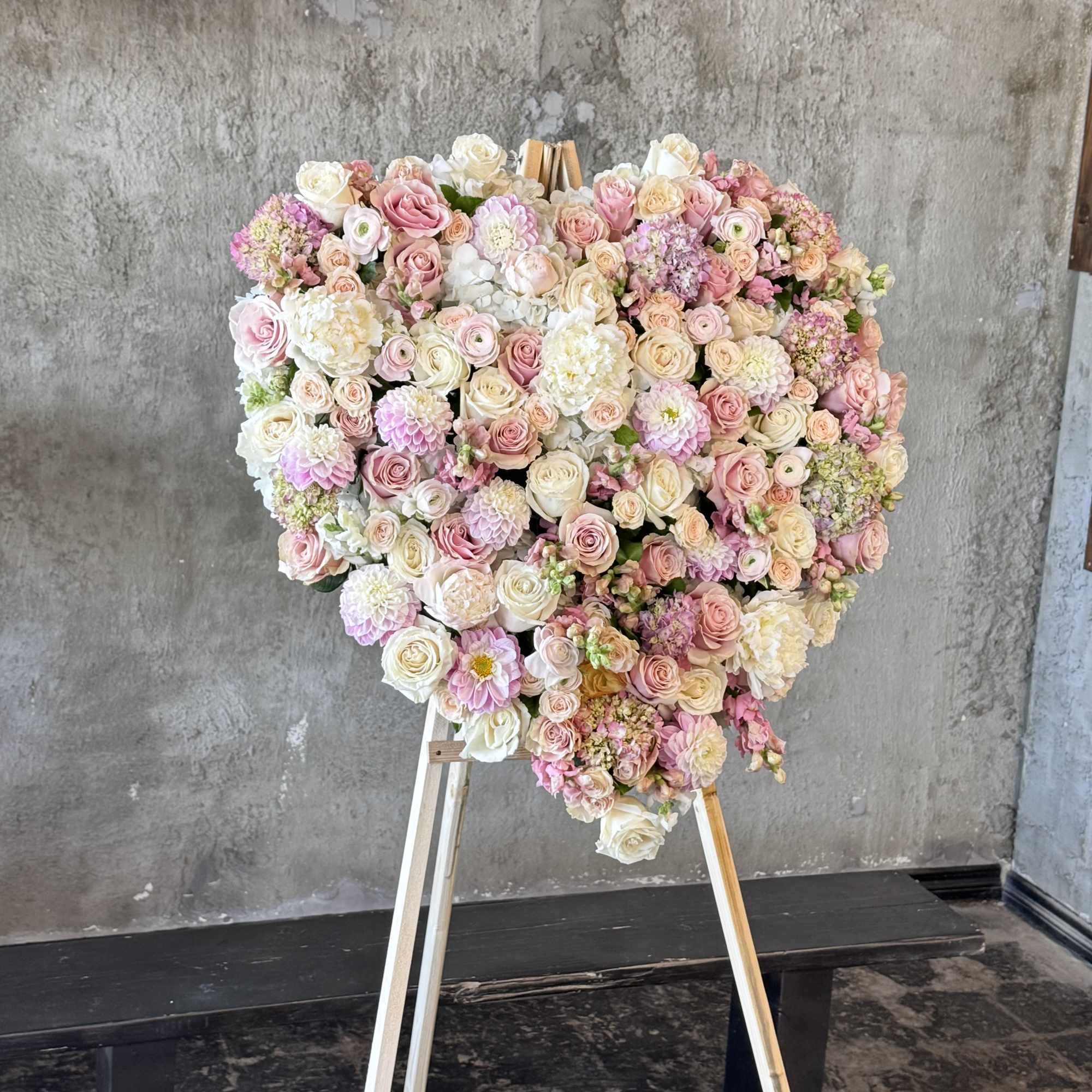Heart-shaped floral arrangement of pink and white roses on an easel