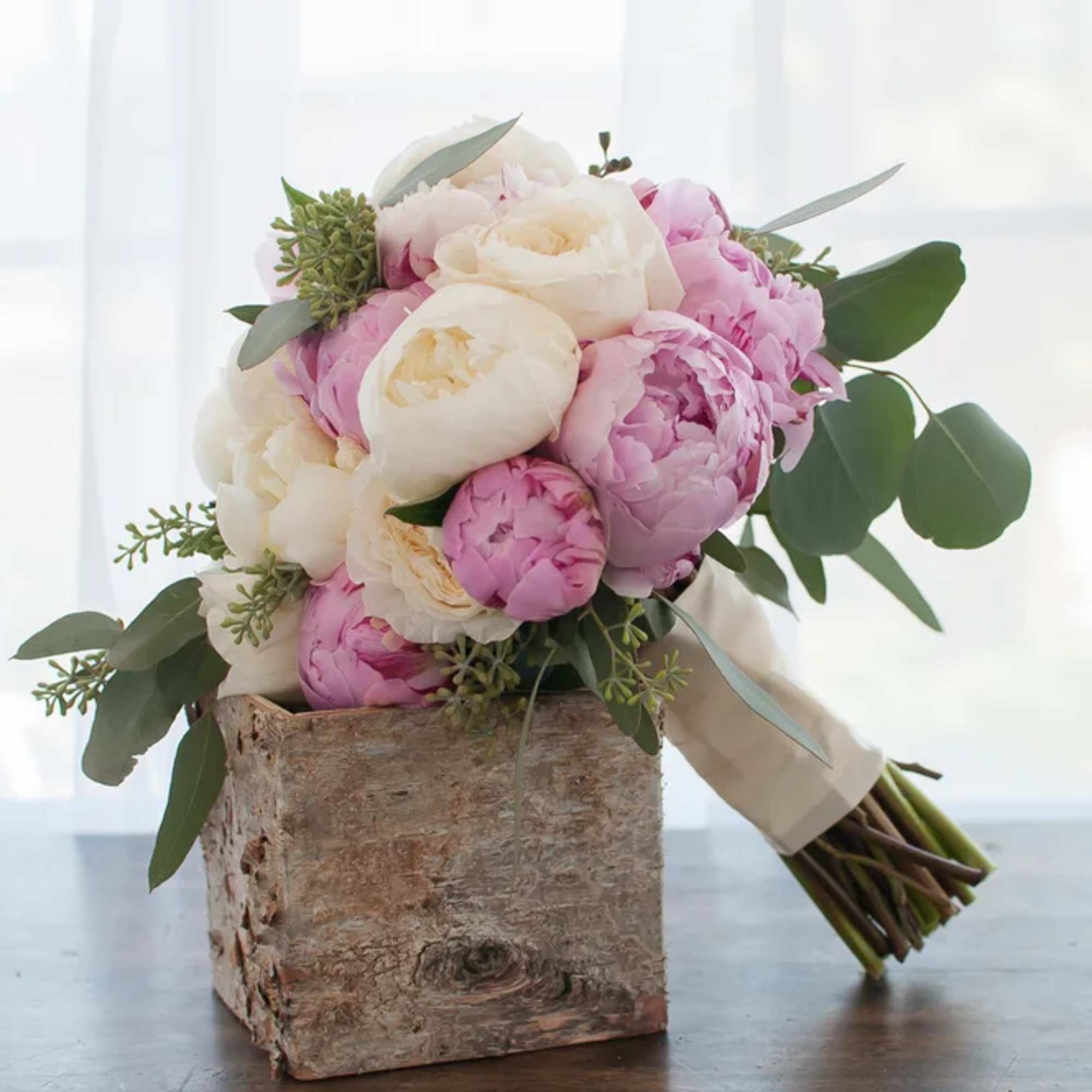 Pink and white peony bouquet with greenery in a rustic wood holder