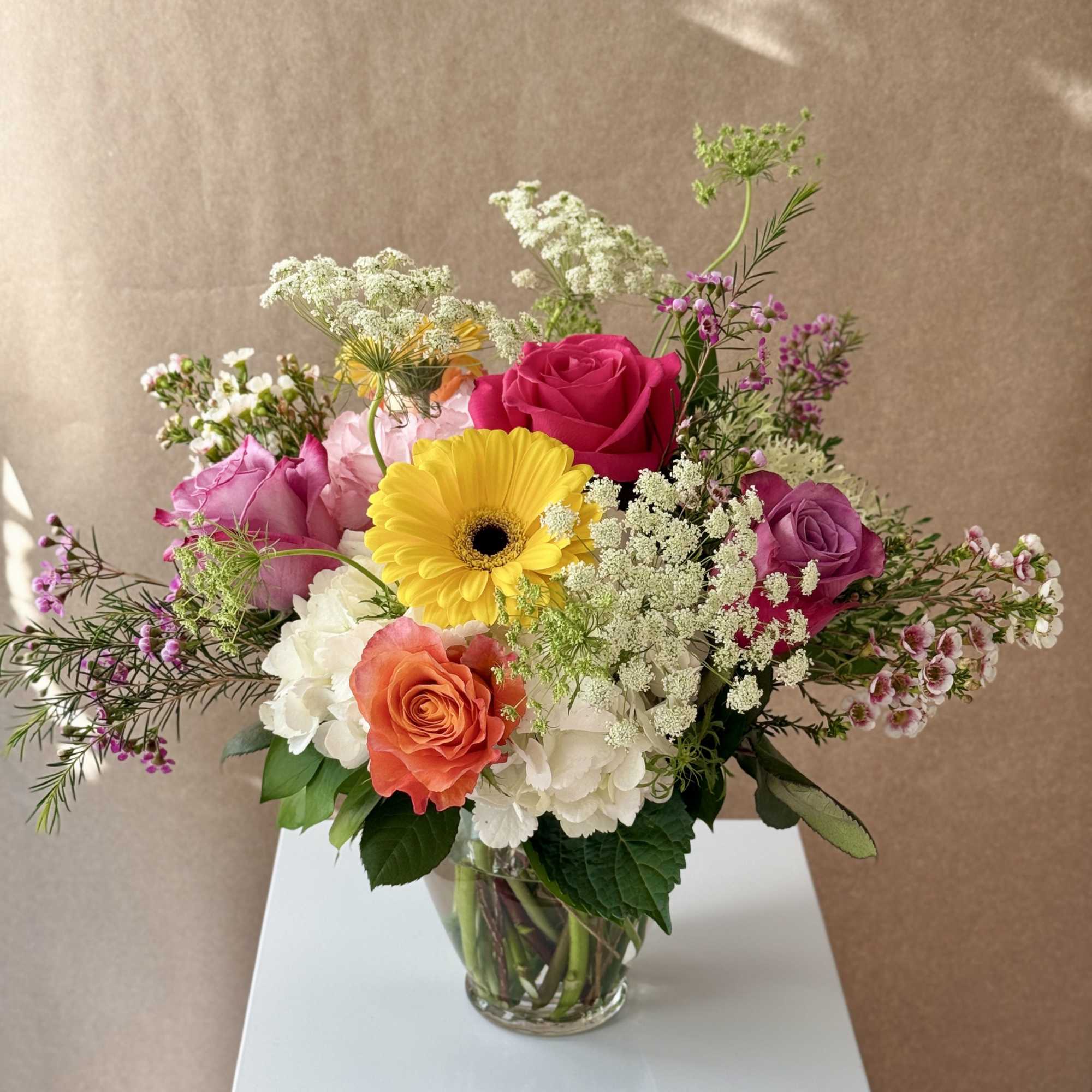 Mixed bouquet of roses, hydrangeas, and a yellow gerbera daisy in a glass vase