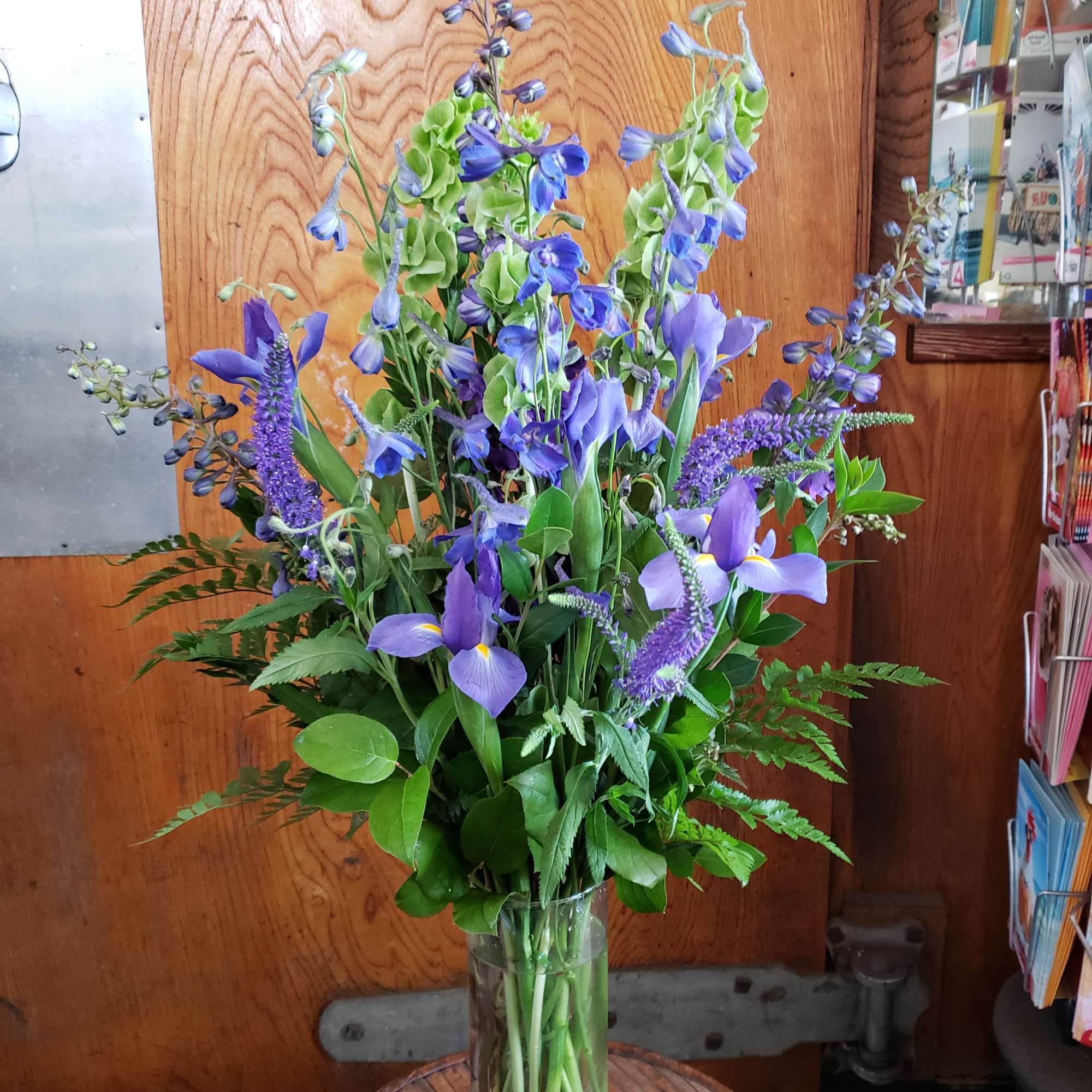 Tall purple and blue floral arrangement in a clear glass vase