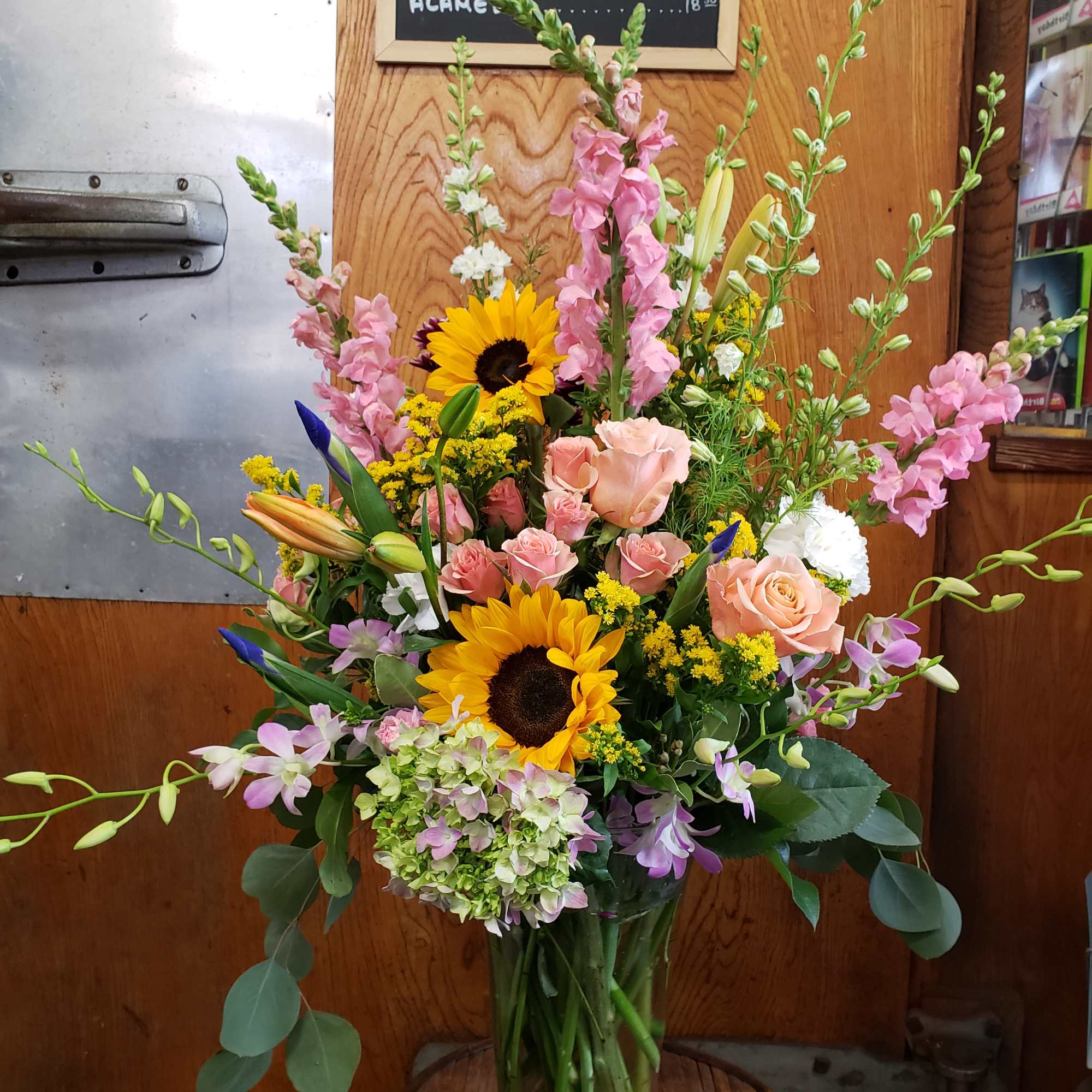 Tall mixed bouquet in a glass vase with sunflowers, roses, and pink blooms
