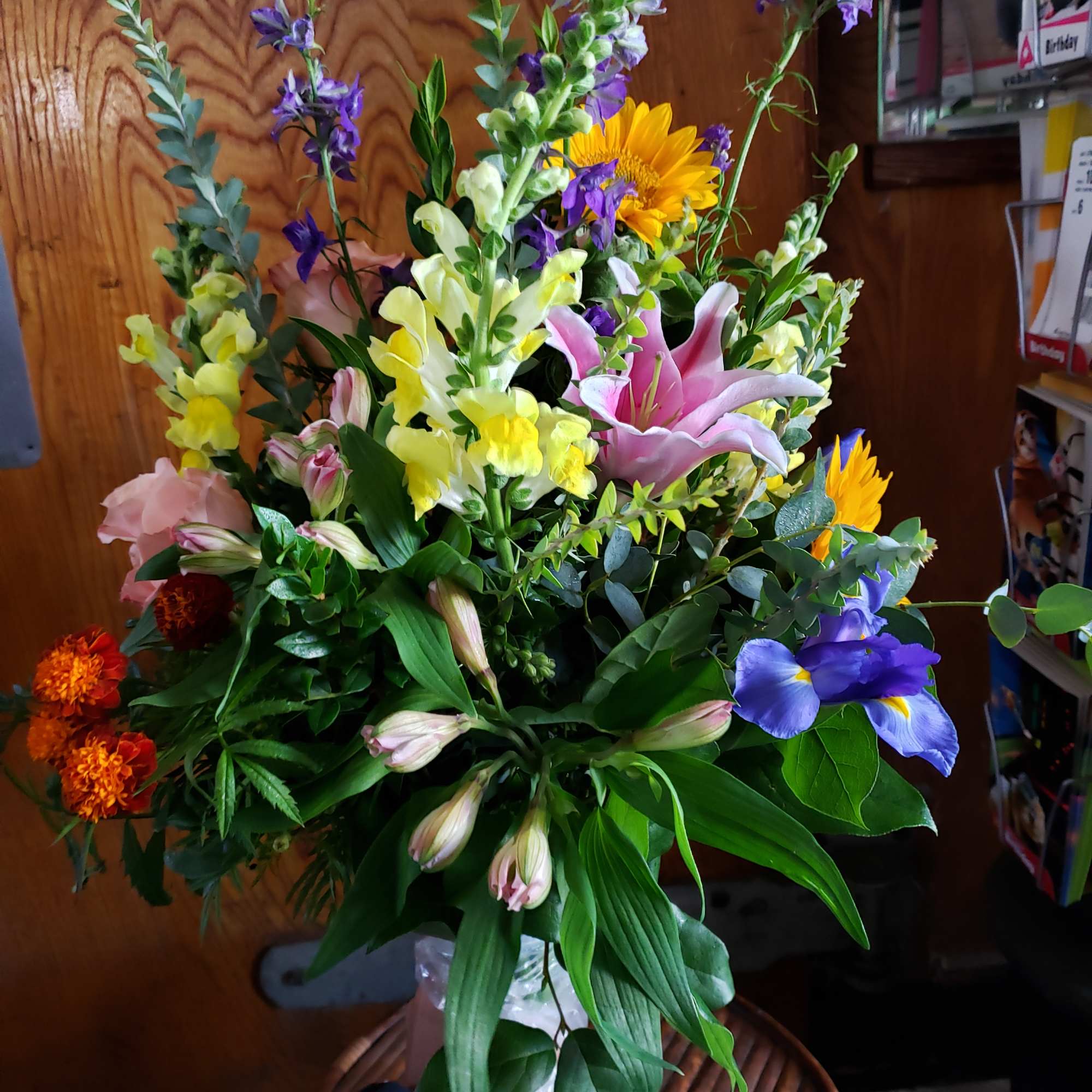 Mixed bouquet with lilies, sunflowers, and purple blooms in a clear vase